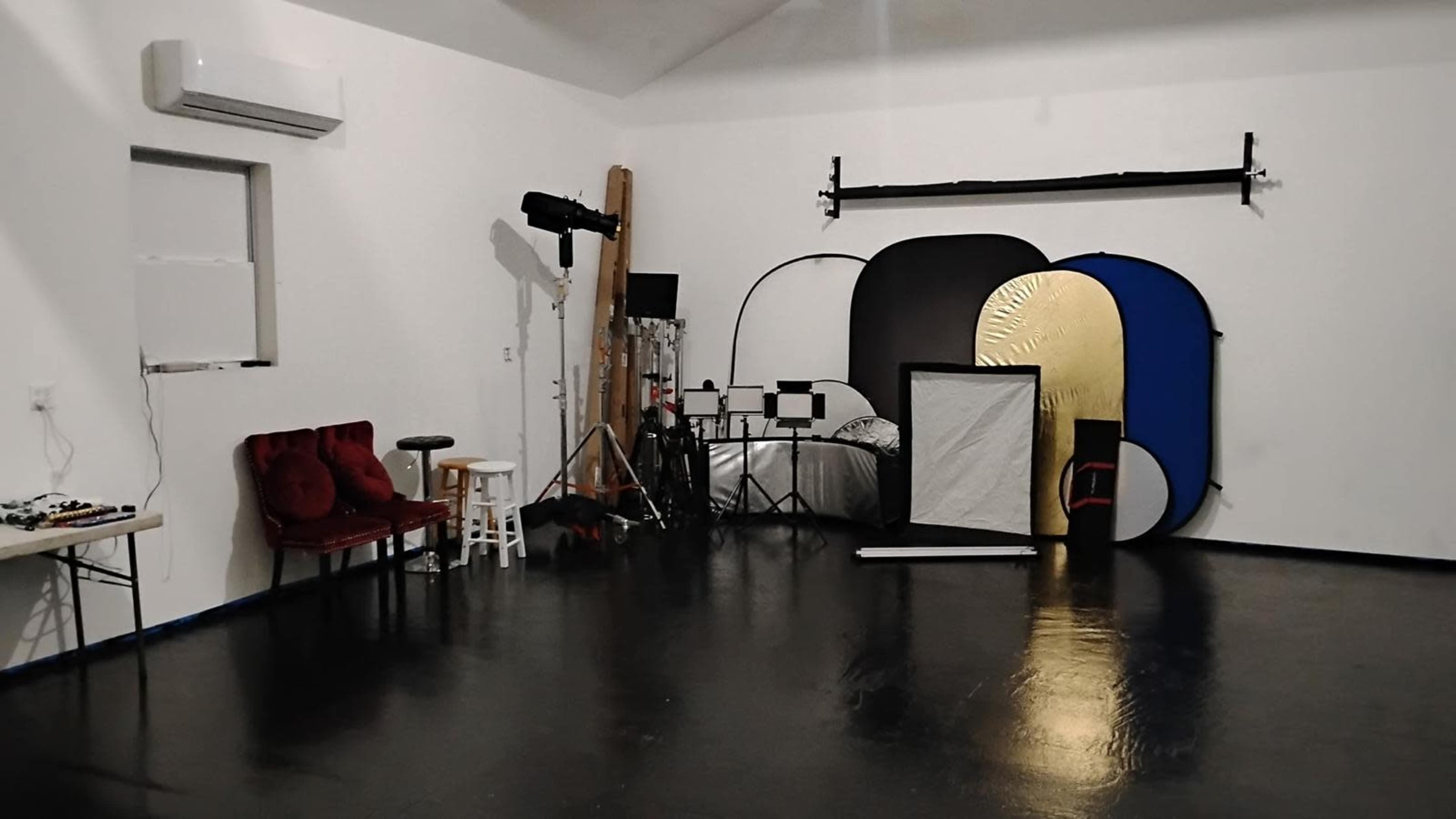 The image shows a photography studio with various backdrops, lighting equipment, and furniture arranged along the walls.
