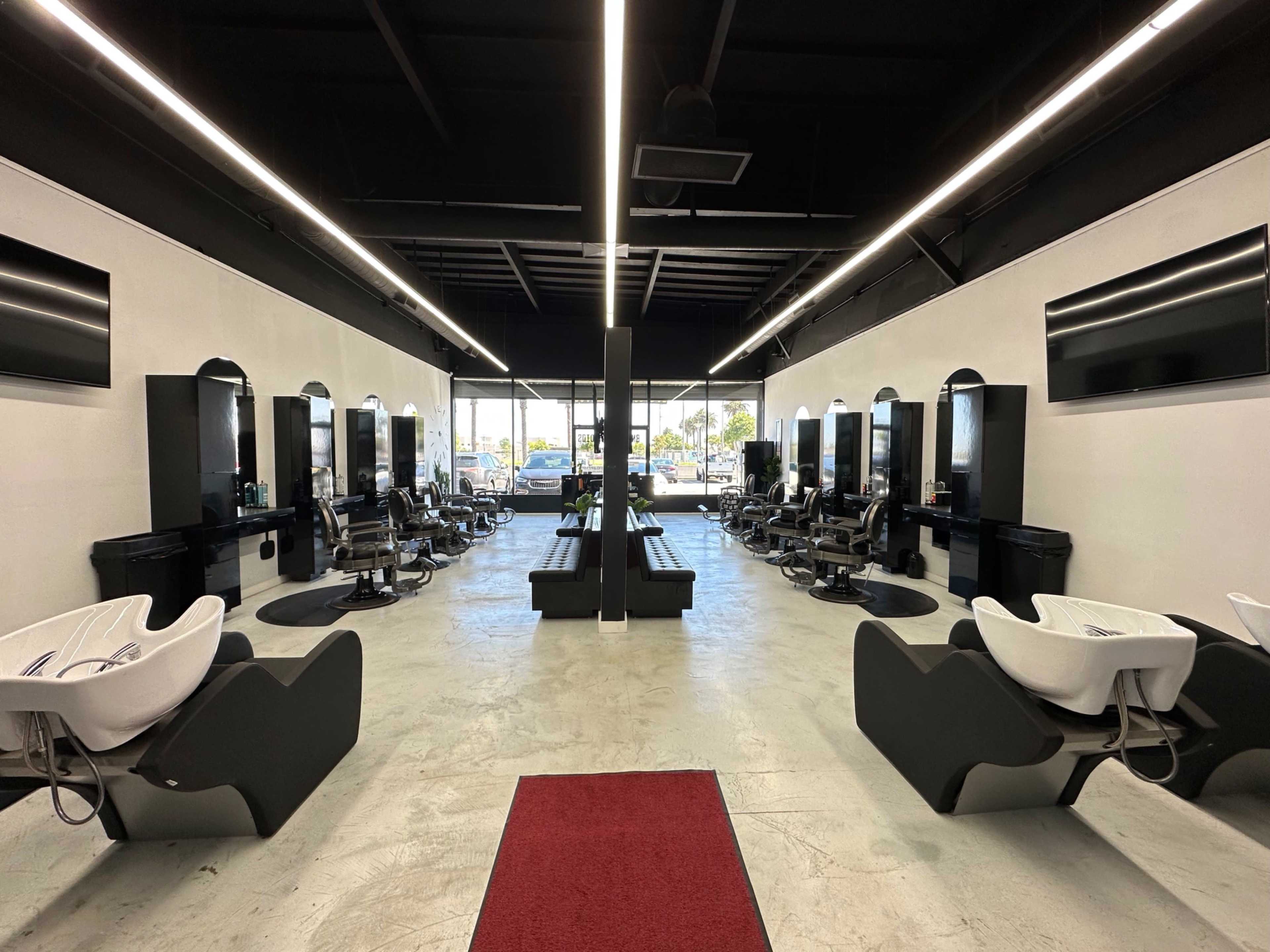 The image shows a modern hair salon interior with styling stations on both sides and a central seating area, illuminated by overhead lights.