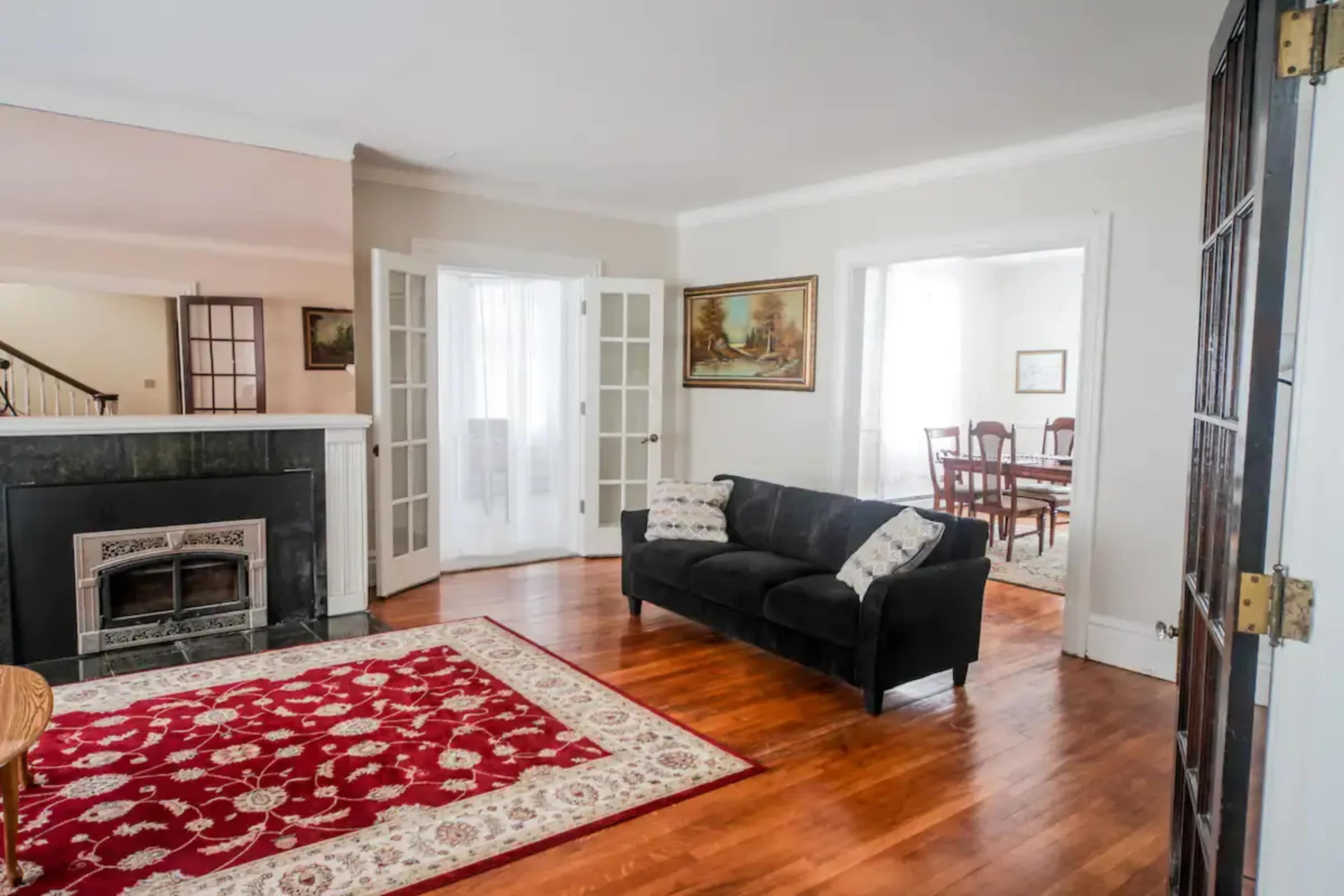 A living room features a black couch on a red rug, with a fireplace and French doors leading to other spaces.