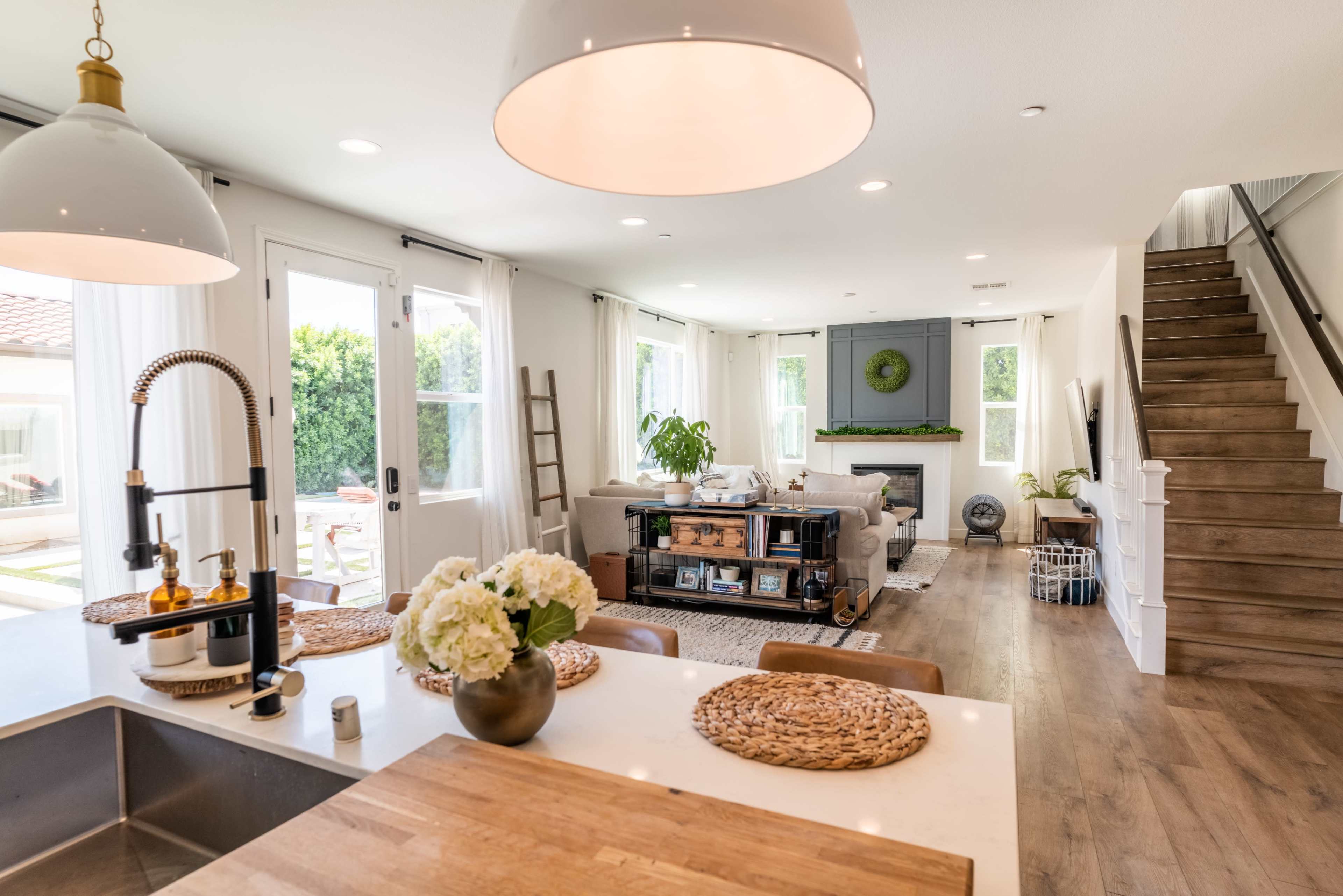 A modern living space features a kitchen island with seating, a cozy seating area with a fireplace, and a staircase leading to an upper level.