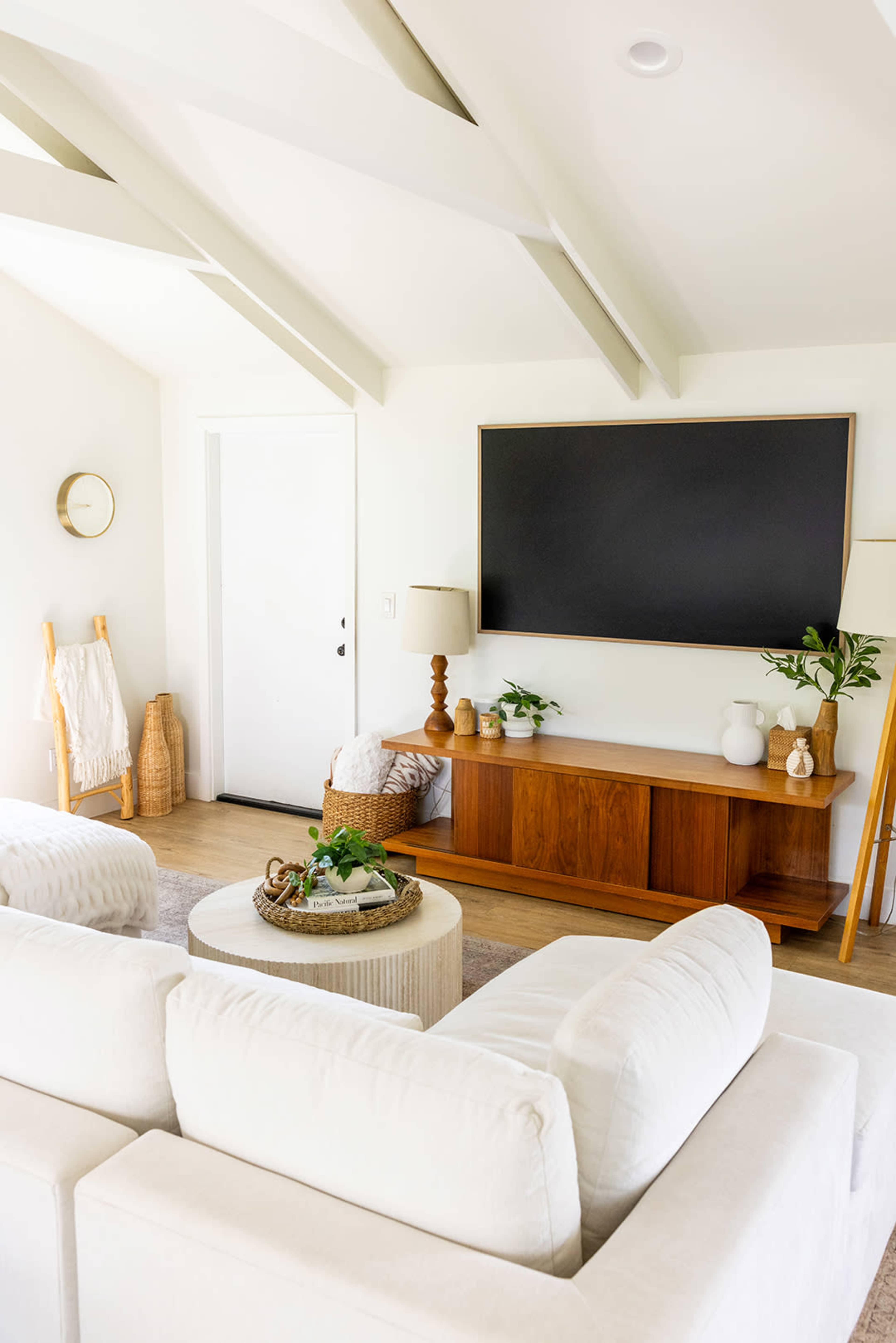 The image shows a bright living room featuring a modern sofa, a wooden TV stand with decorative items, and a door leading outside.