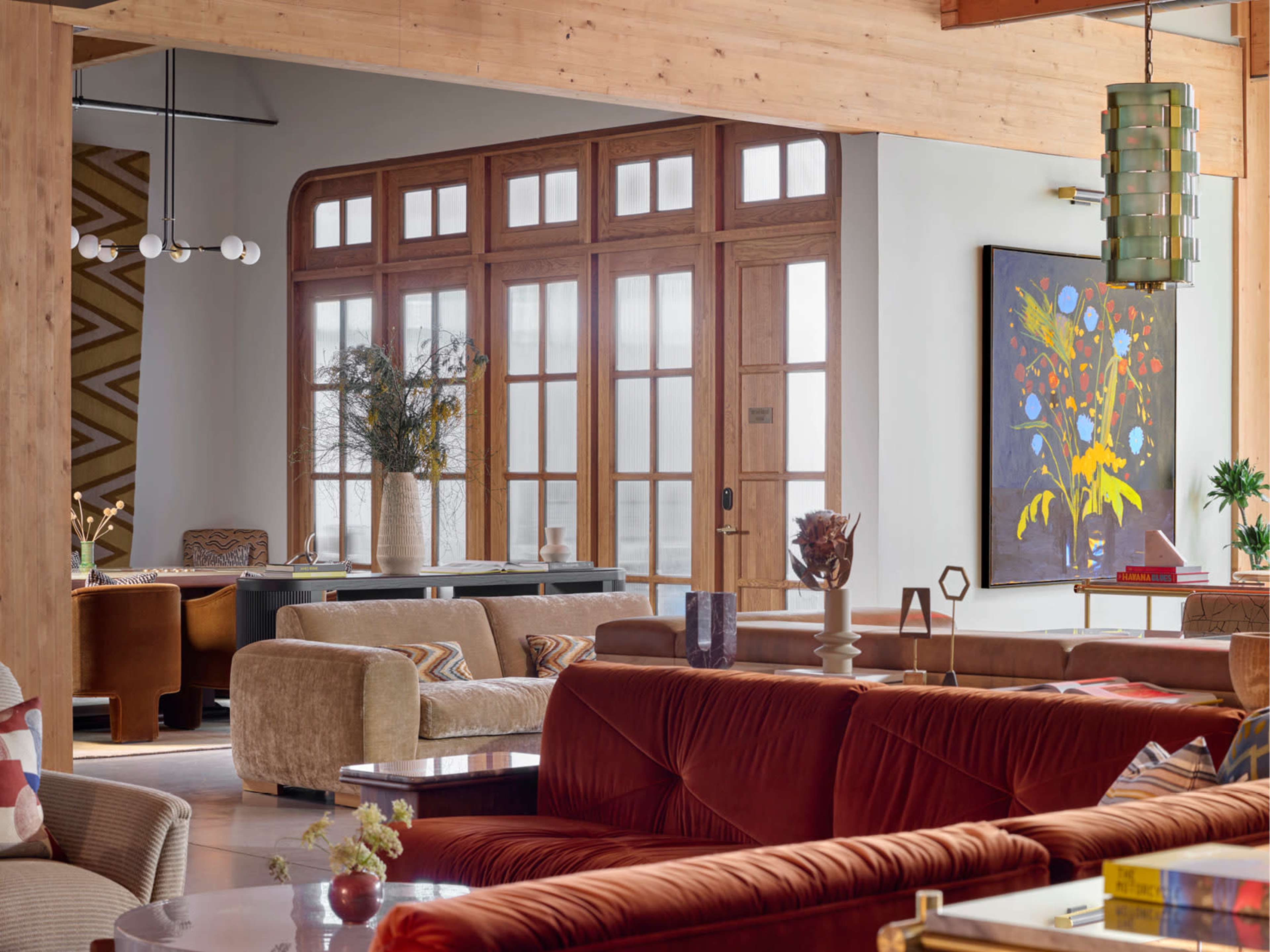The interior of a spacious, modern living area features wooden doors, stylish furniture, and a colorful artwork on the wall.