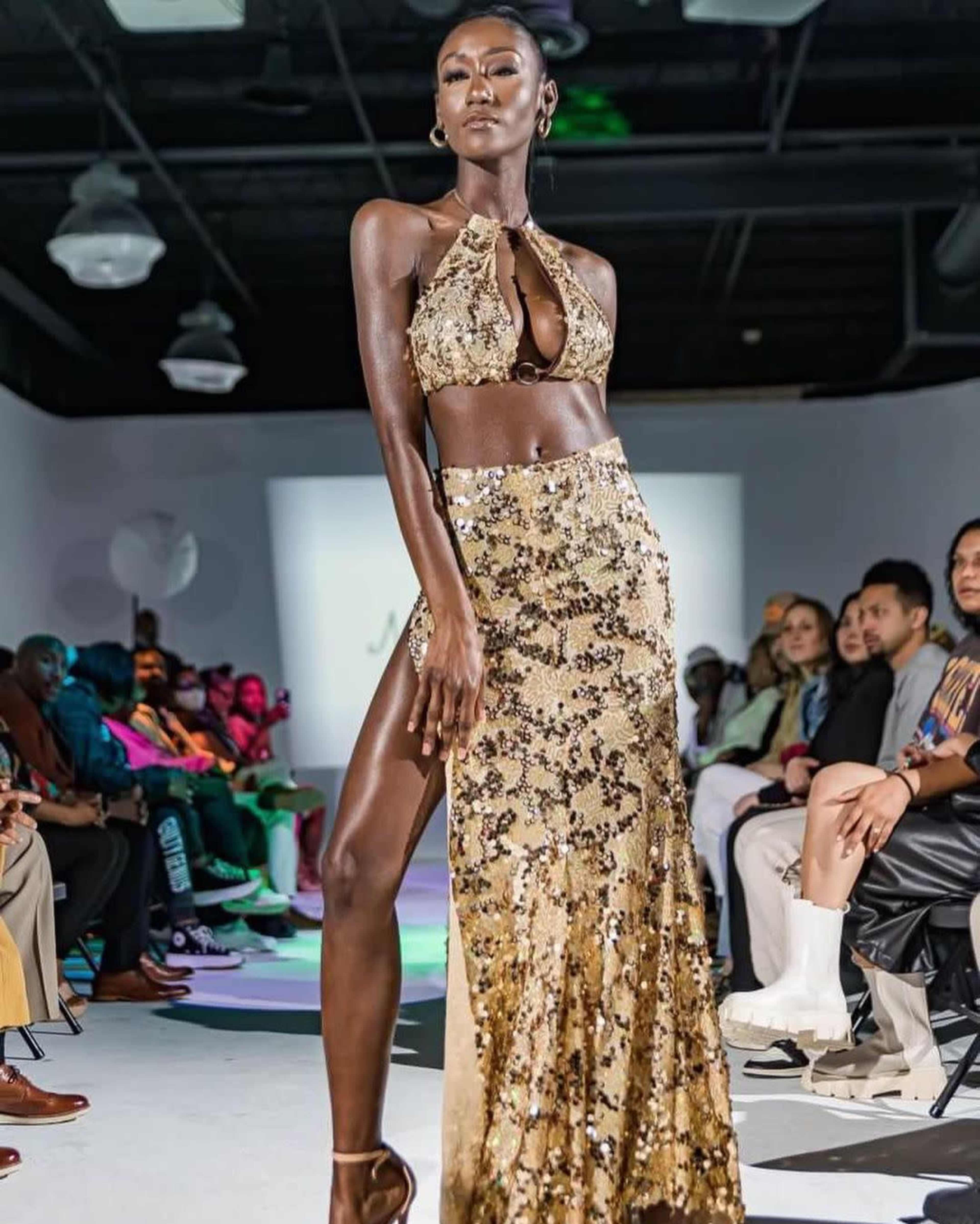 A model walks down a runway in a sparkling gold two-piece outfit during a fashion show.