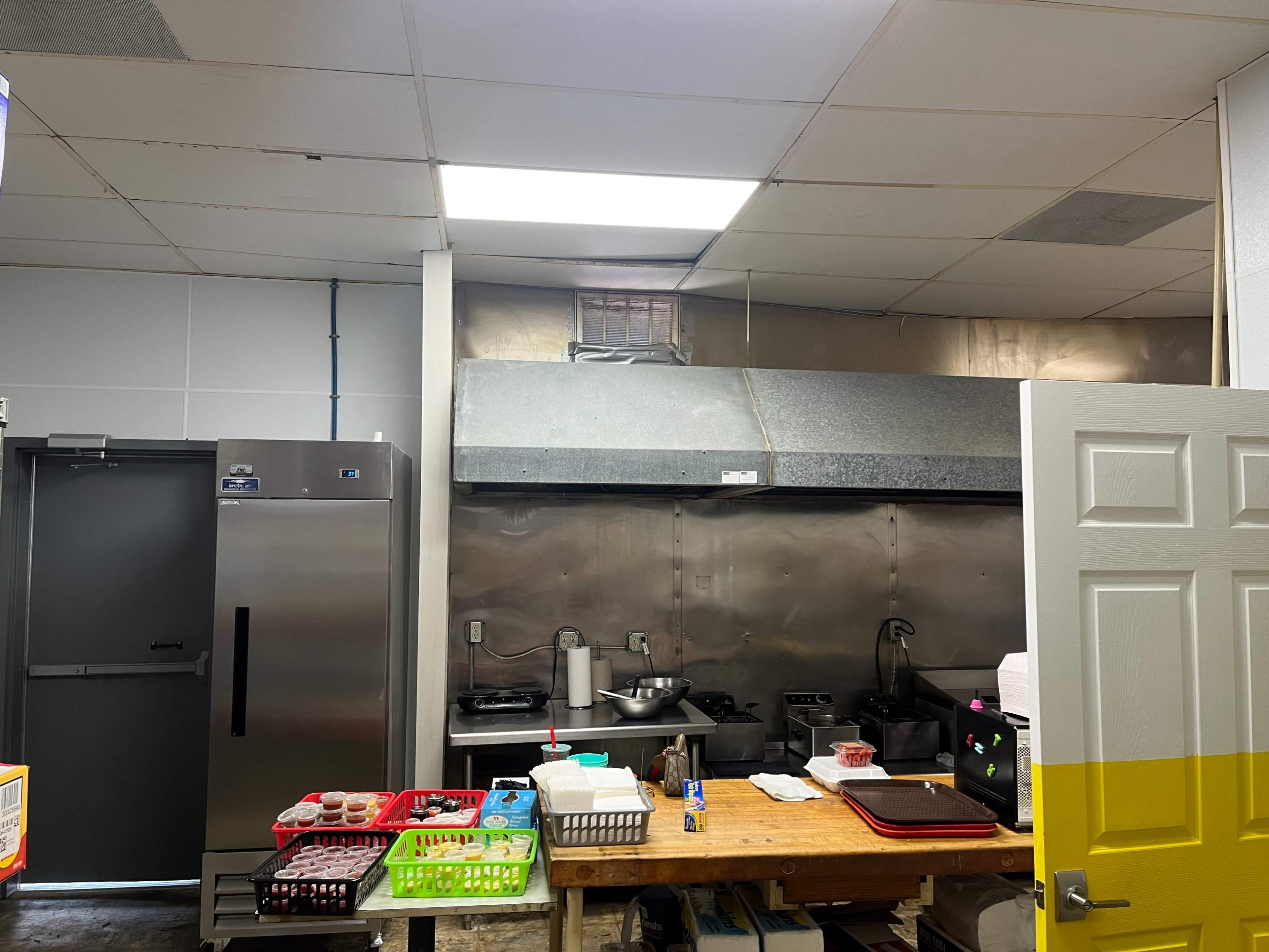 A commercial kitchen featuring stainless steel appliances, a ventilation hood, and a countertop with various kitchen tools and containers.