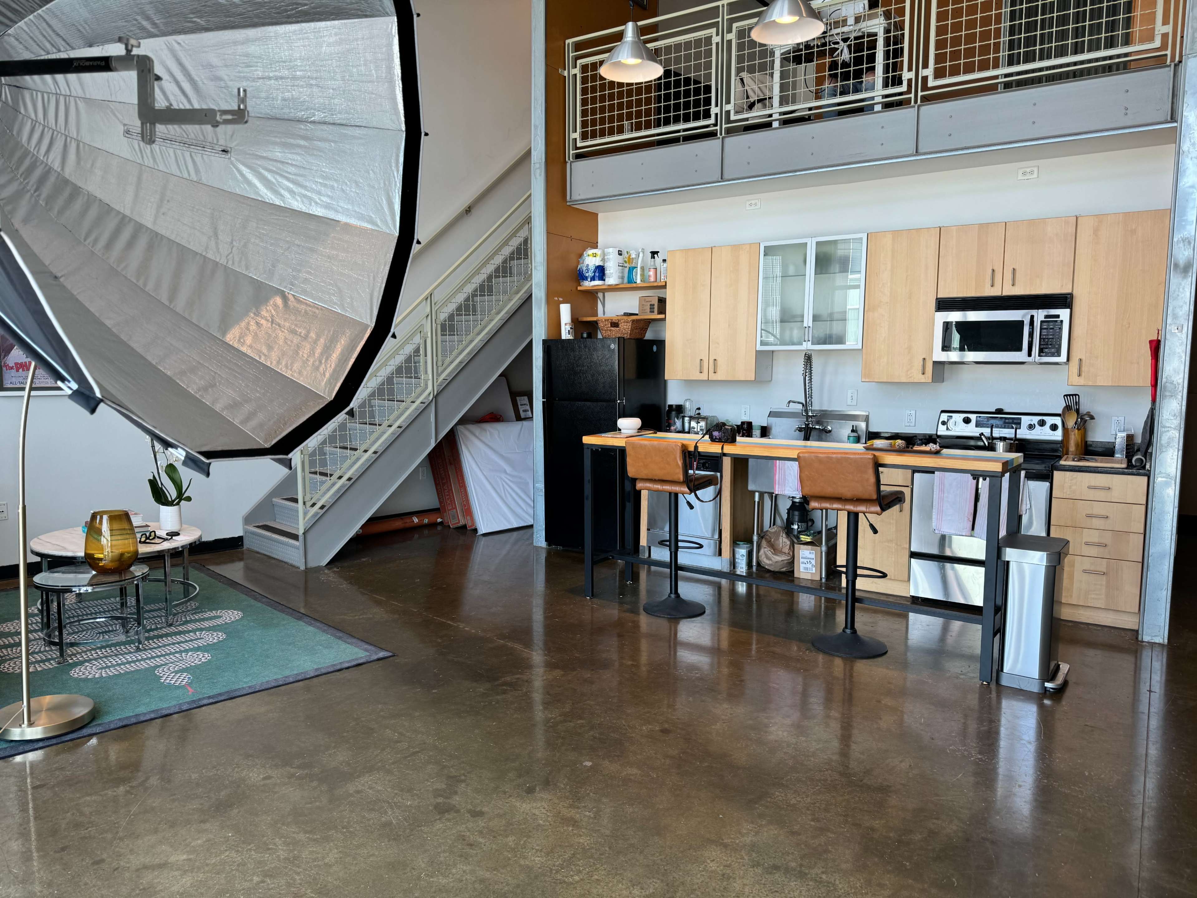 A spacious loft with a kitchen area, a dining table, and a large lighting umbrella positioned in the foreground.