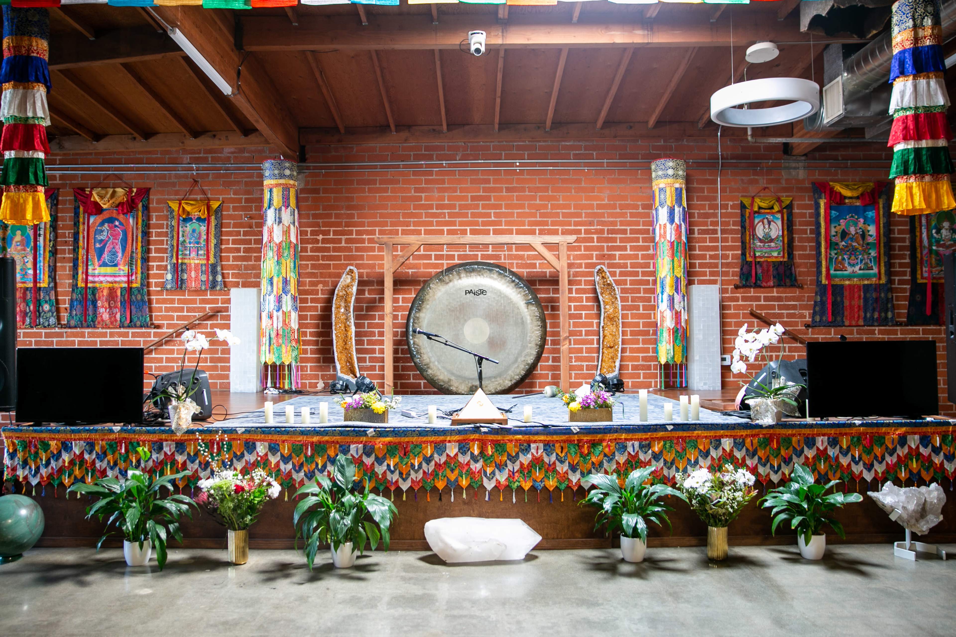 A decorated stage with a large gong at the center, surrounded by potted plants and colorful banners hanging from the walls.