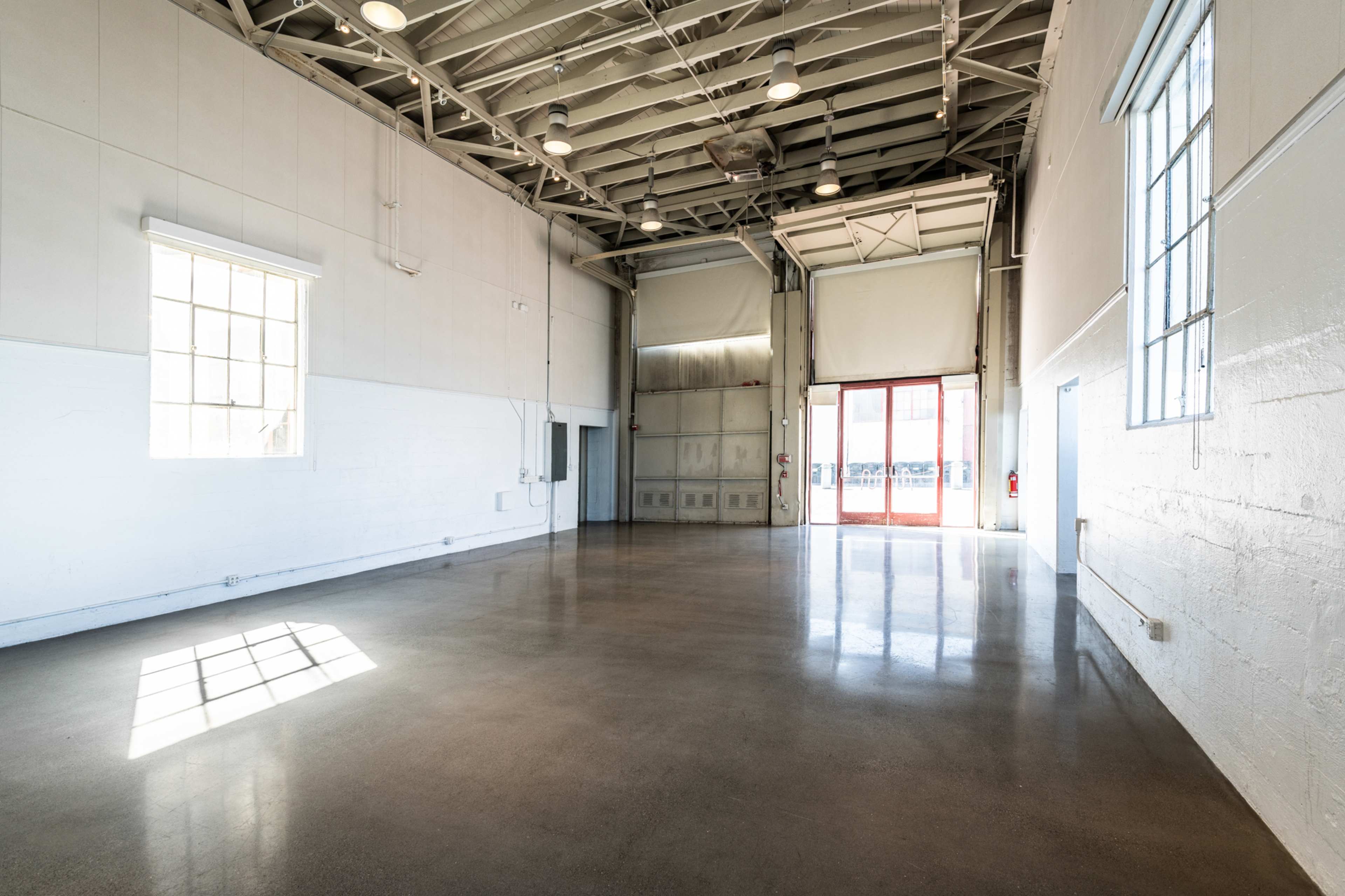 A spacious, empty industrial warehouse with polished concrete floors and large windows letting in natural light.