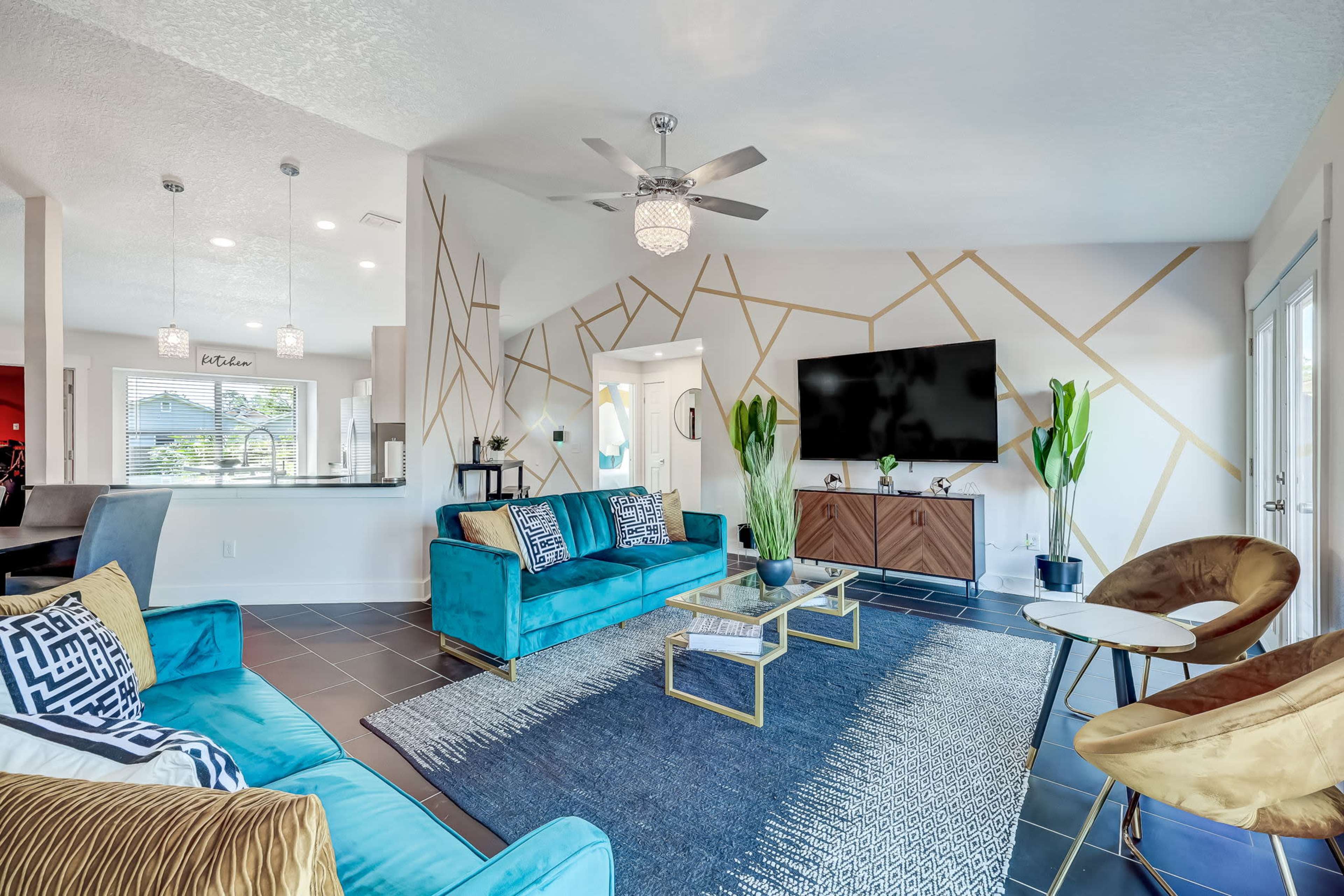 The living room features turquoise sofas, a geometric accent wall, a large television, and decorative plants.