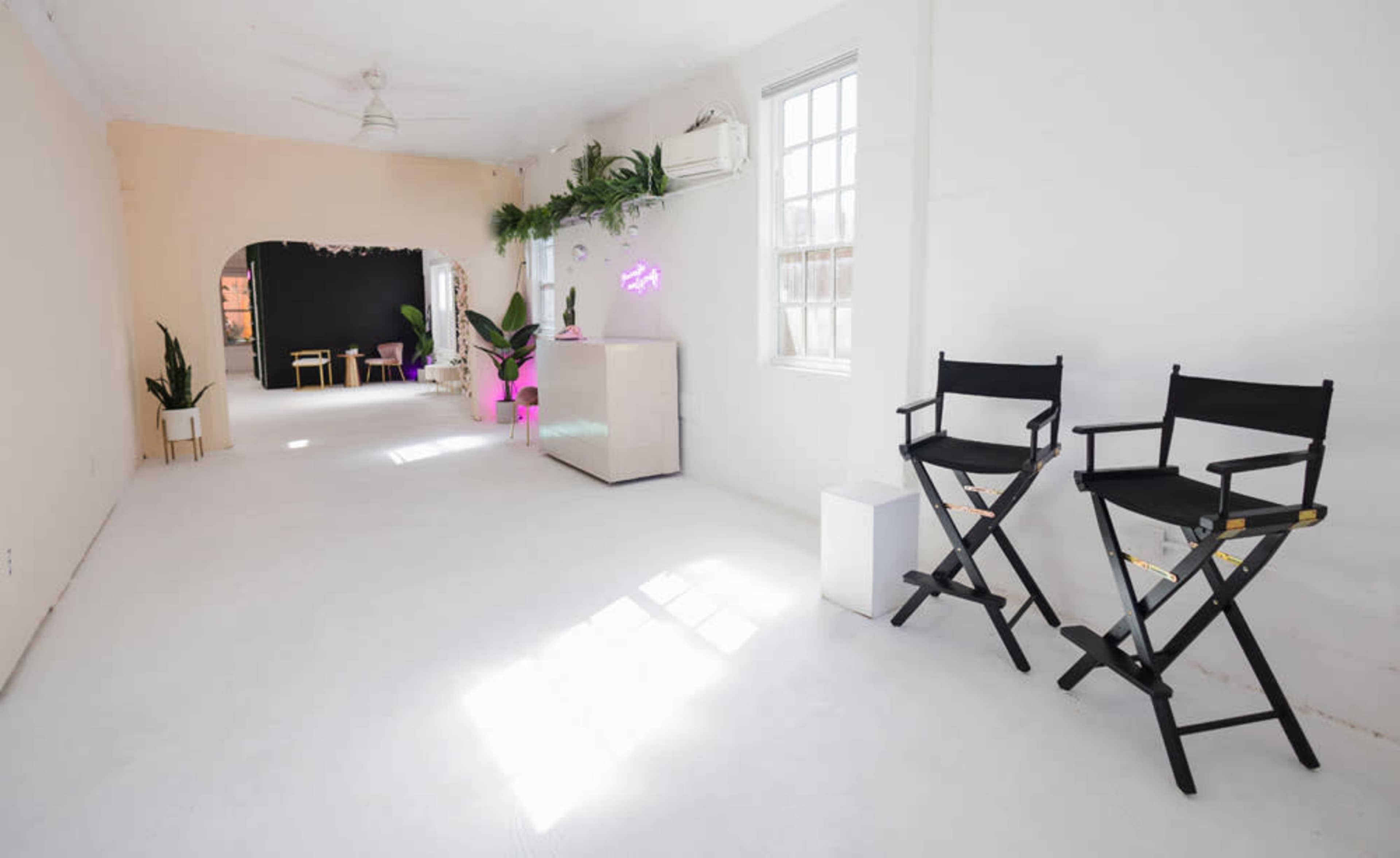 A bright, minimalistic indoor space with two director's chairs, a white cabinet, and plants, illuminated by natural light.