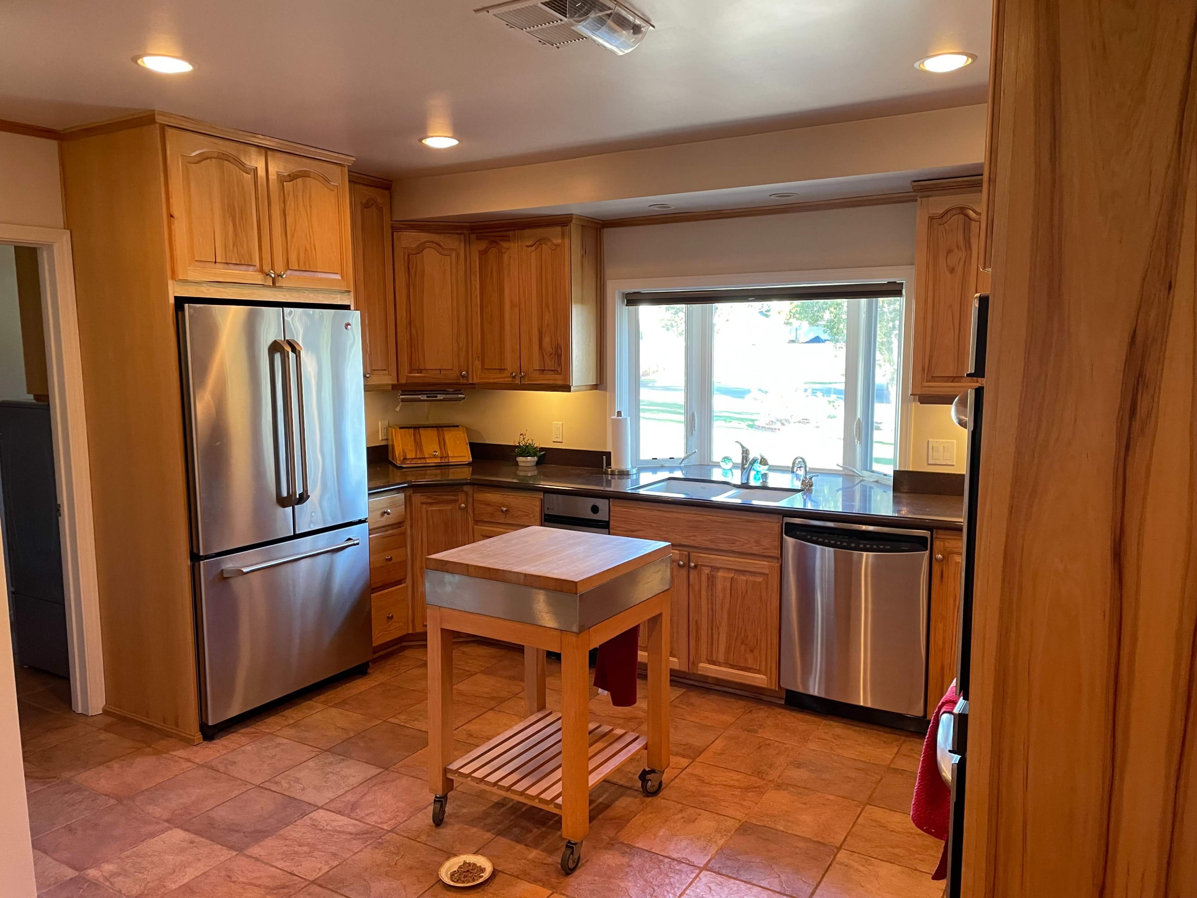 A modern kitchen features wooden cabinets, stainless steel appliances, and a central island with wheels.