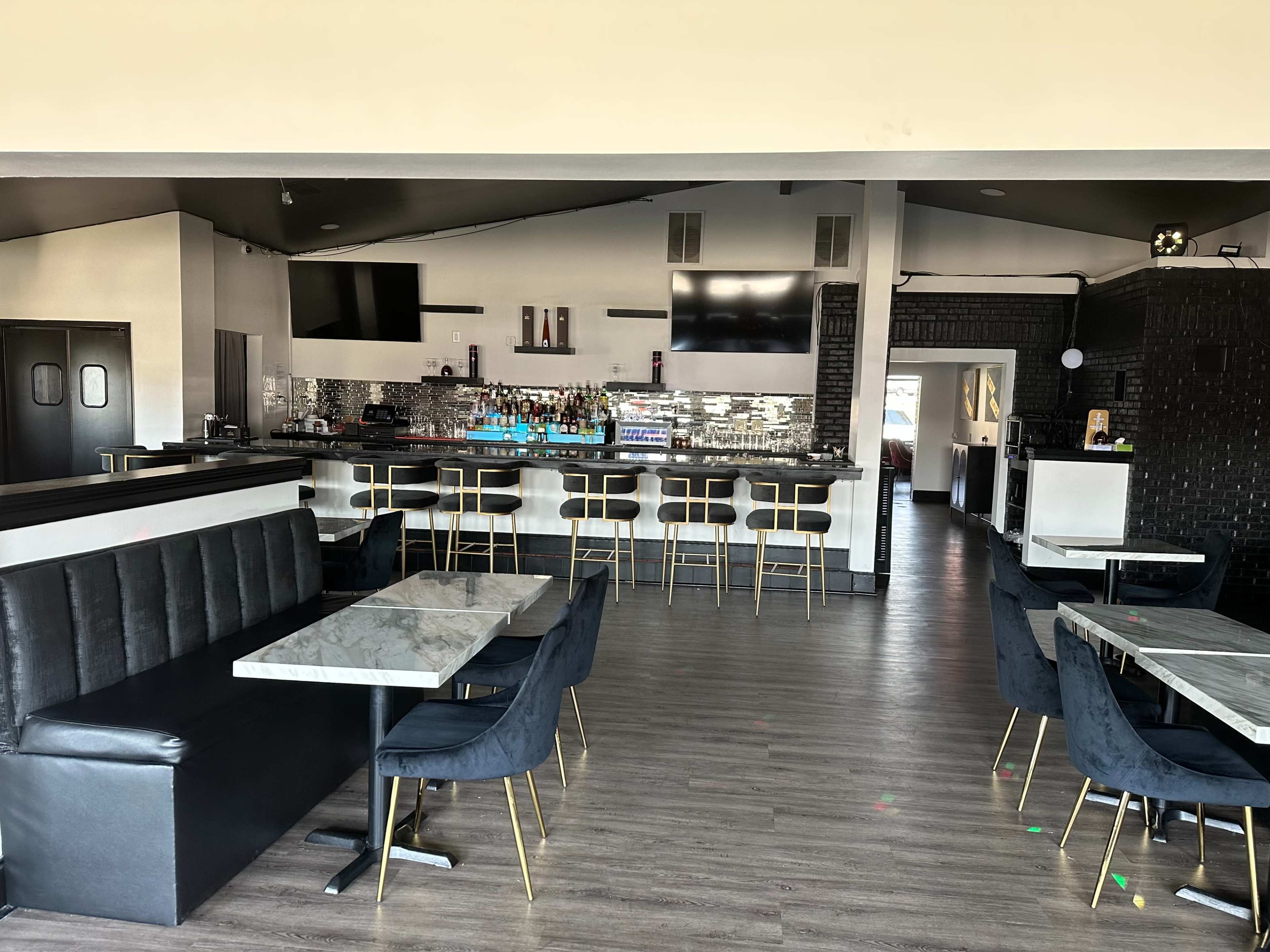 The interior of a modern restaurant features a sleek bar area with high stools, marble-topped tables, and a mix of dark and light decor.