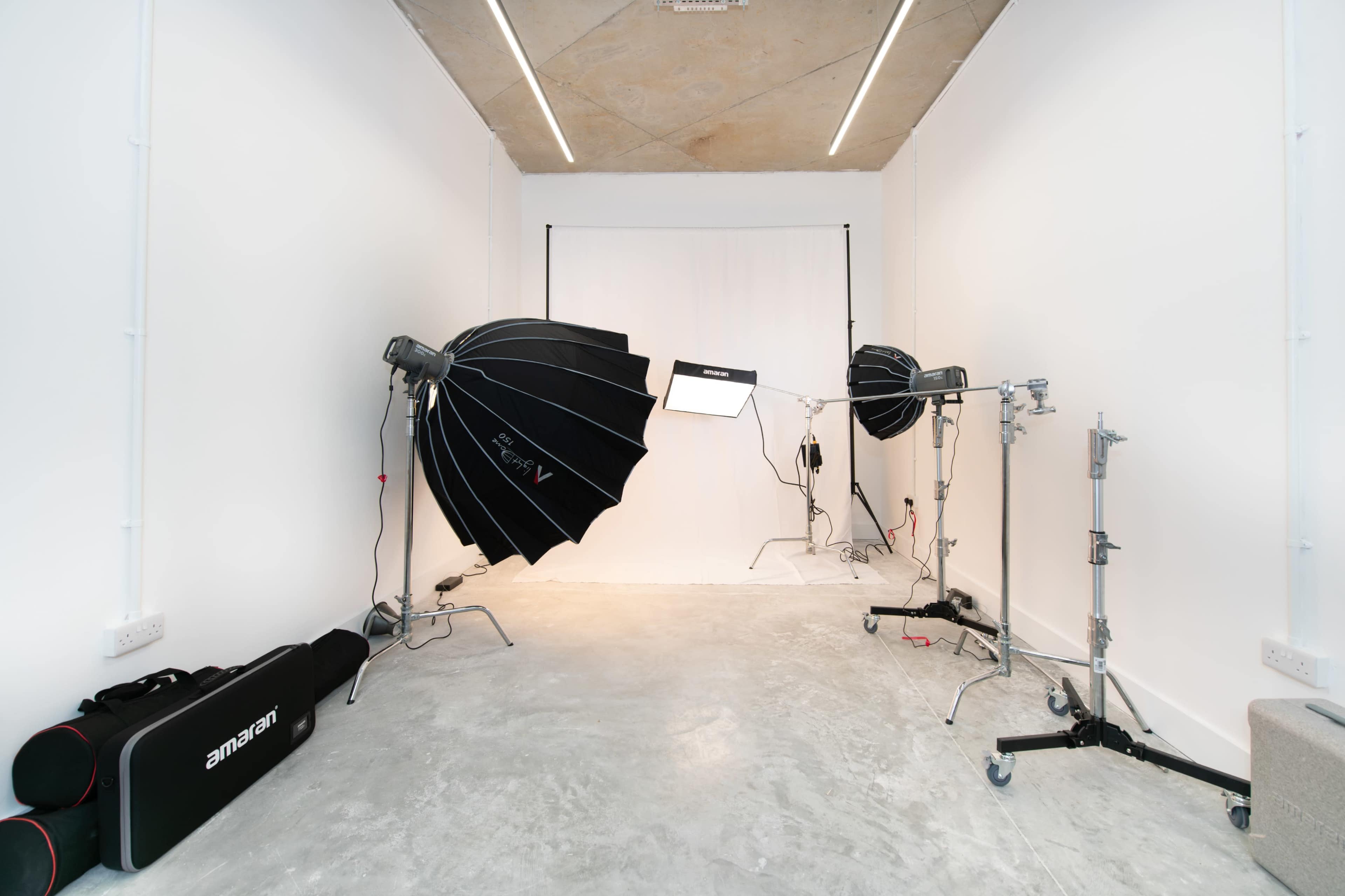 A photography studio features two large softbox lighting setups and a plain white backdrop against a concrete floor.