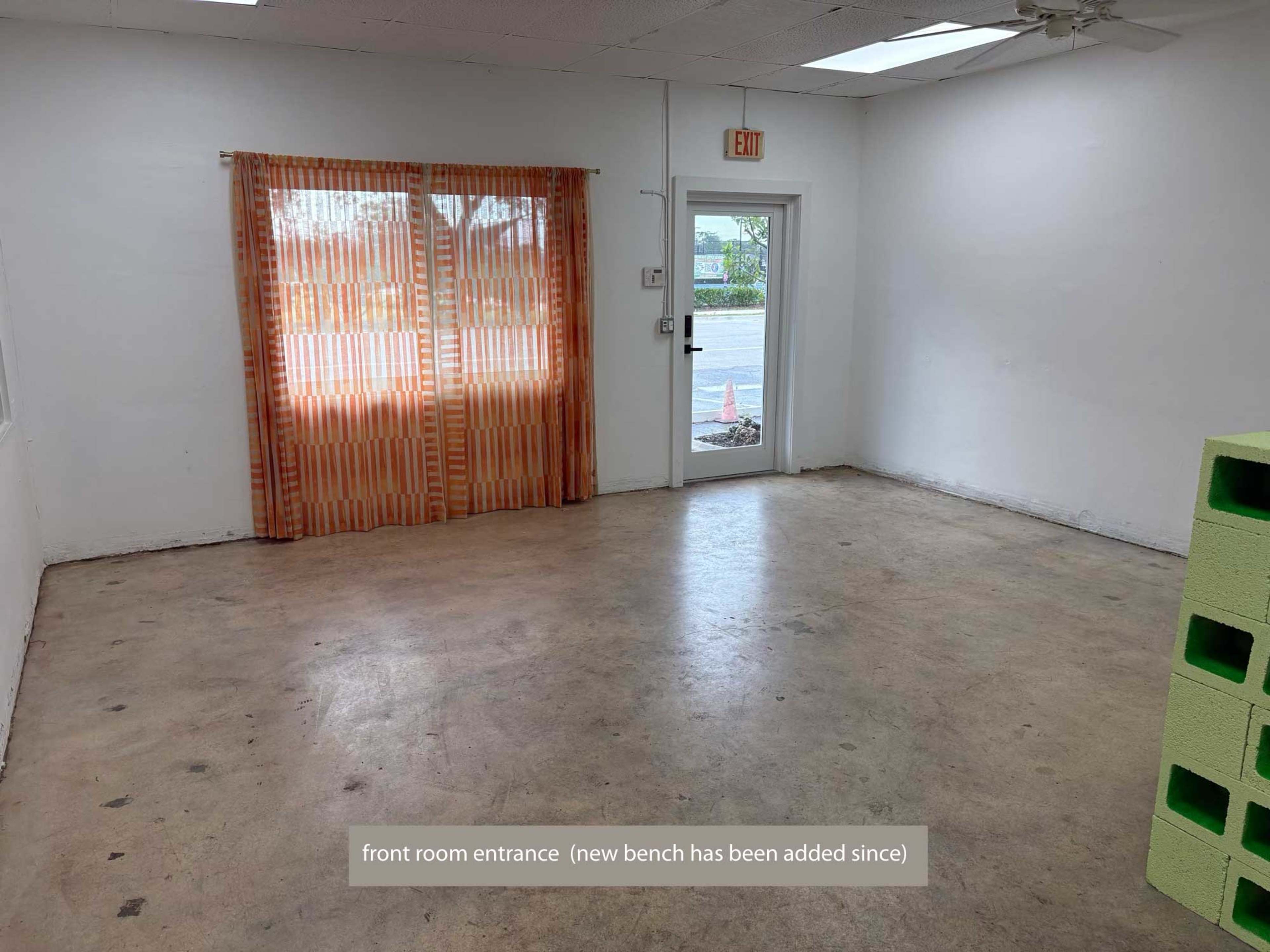 The image shows a vacant room with a concrete floor, a window covered by orange sheer curtains, and a door leading outside.