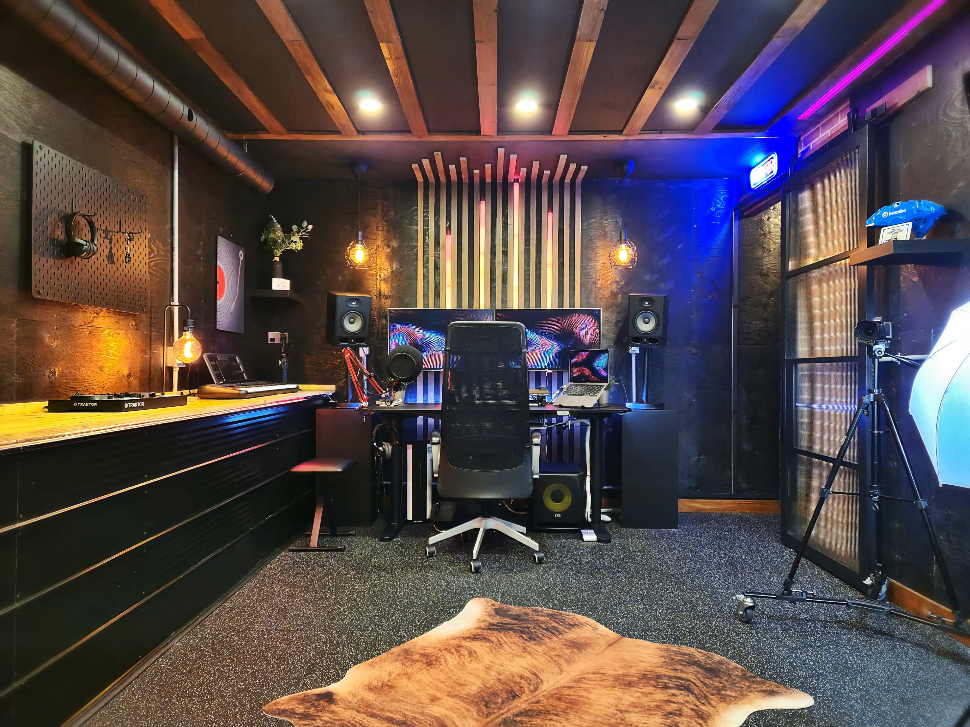 The image shows a dimly lit music production studio featuring a desk with audio equipment, speakers, and a modern chair, complemented by decorative elements on the walls.