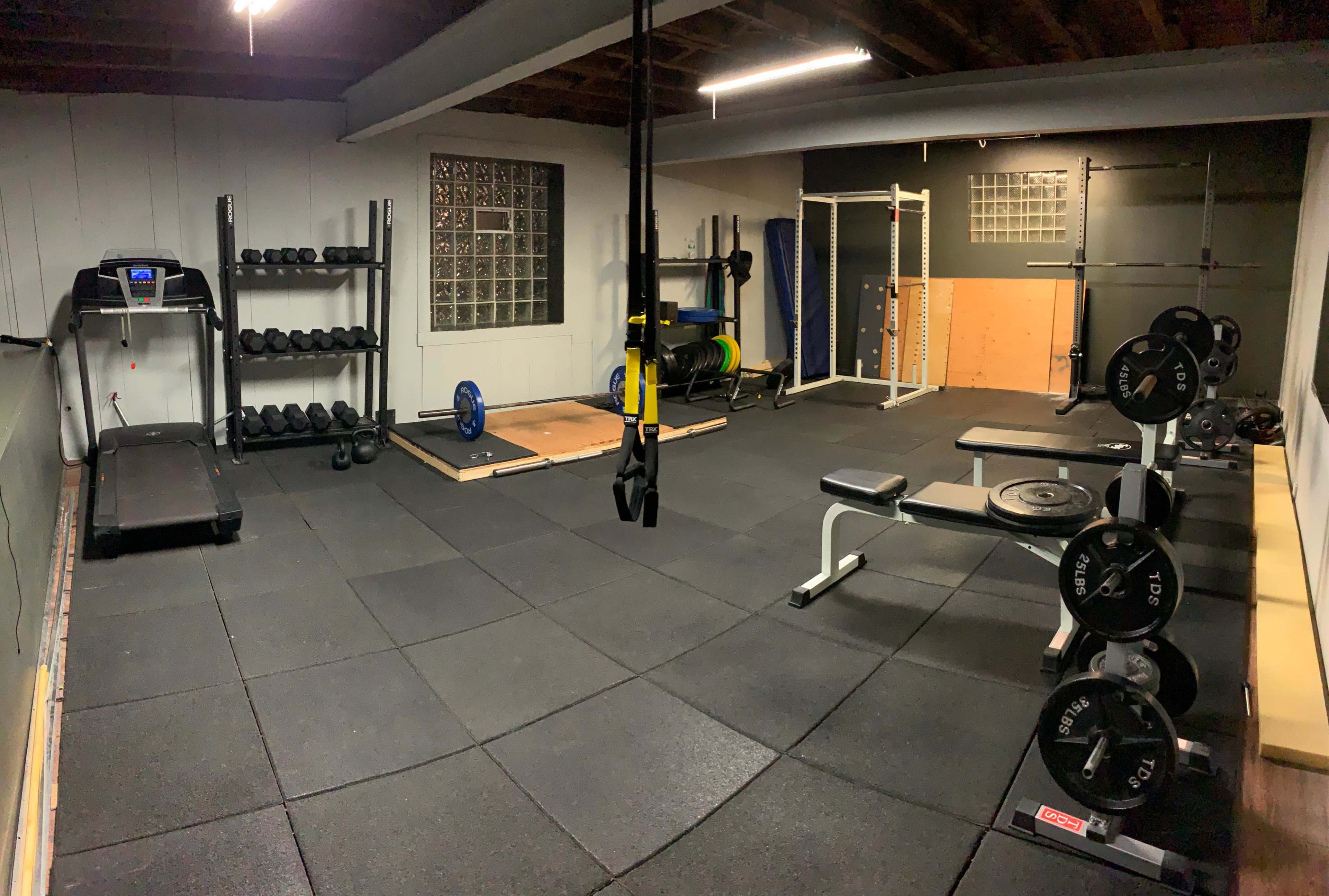 A home gym with various fitness equipment, including dumbbells, a treadmill, a weight bench, and resistance bands set on a rubber floor.