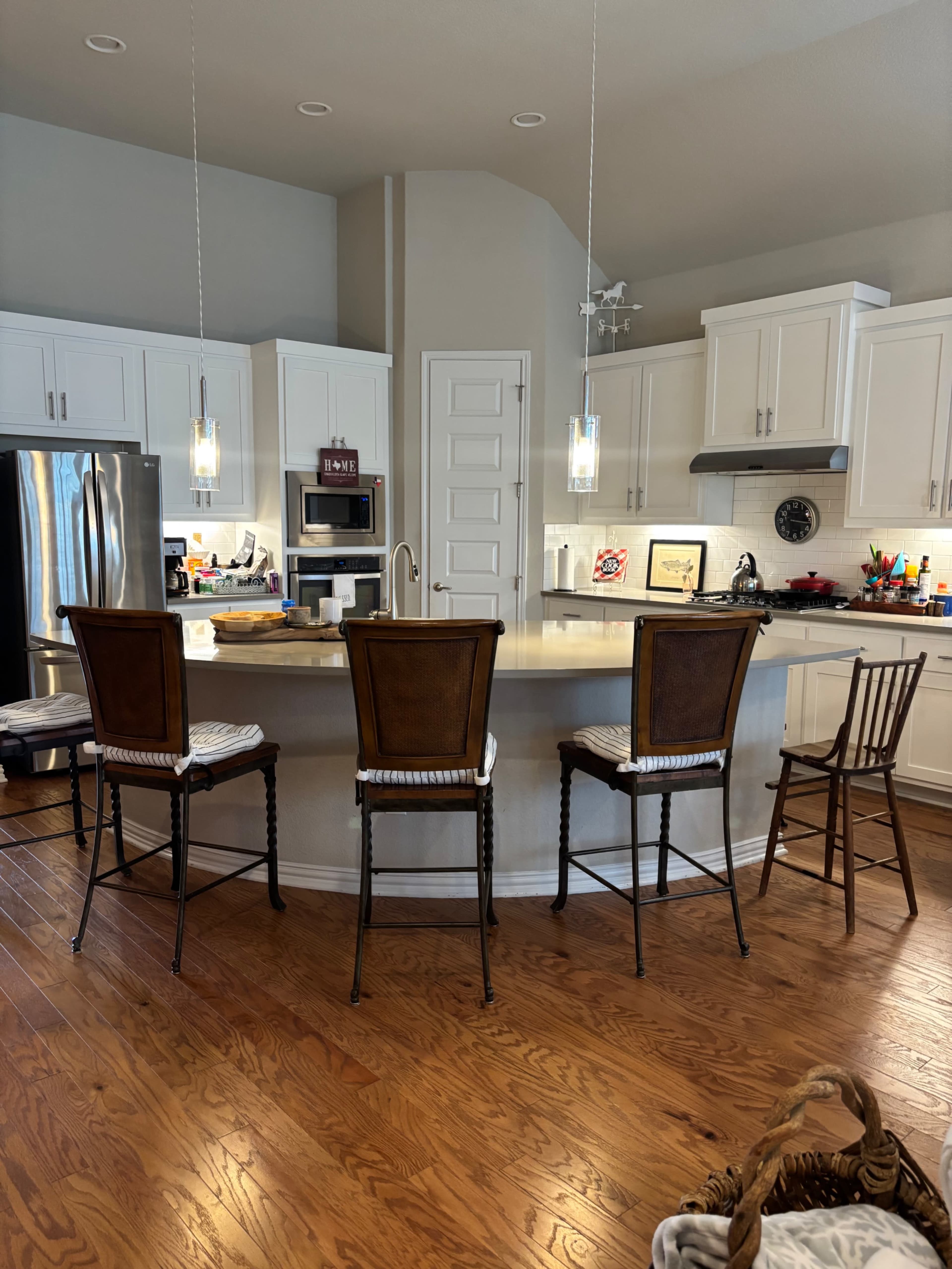 A modern kitchen features a large island with bar stools, stainless steel appliances, and pendant lighting.