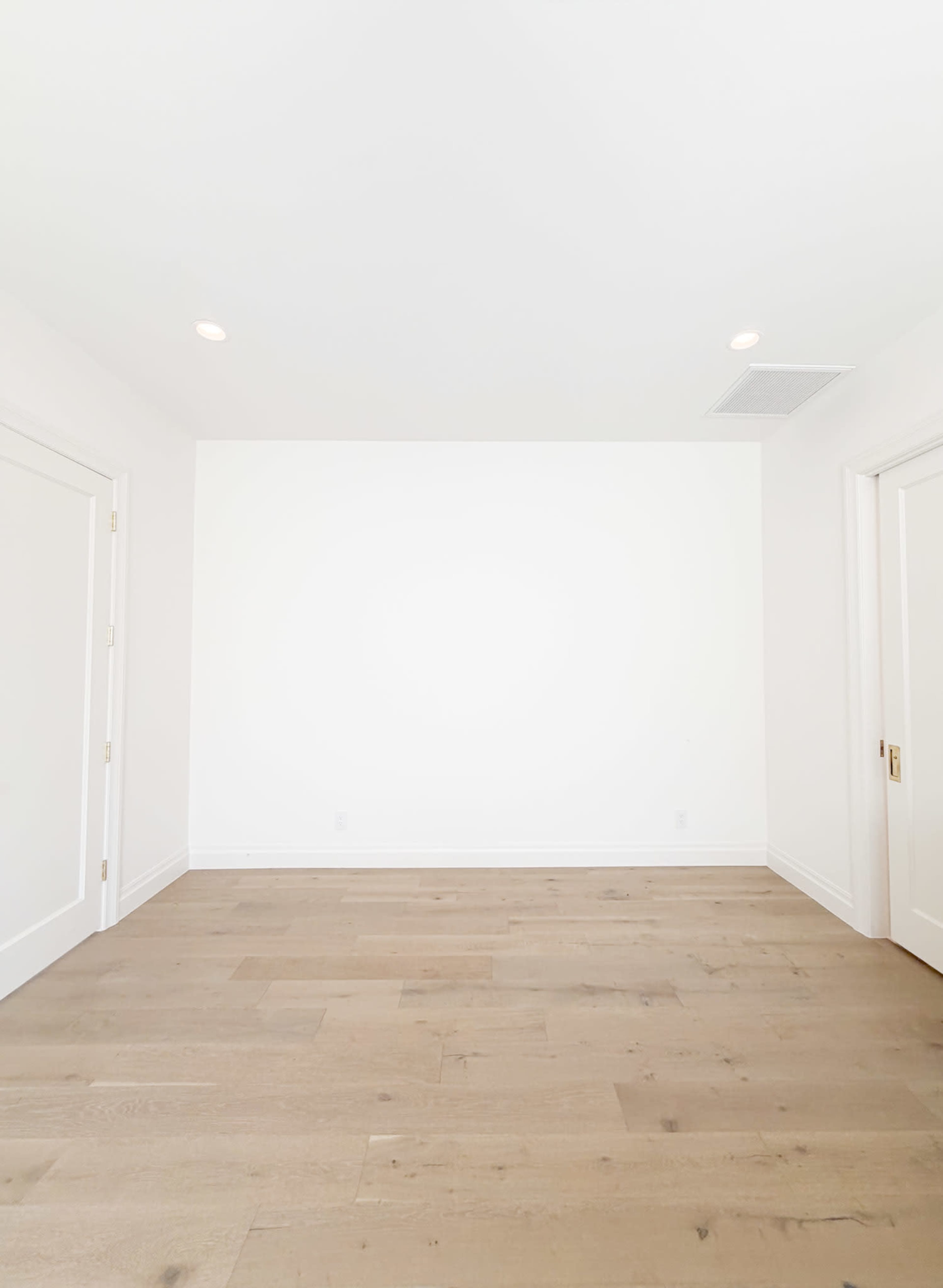 The image shows an empty room with light wood flooring and white walls.