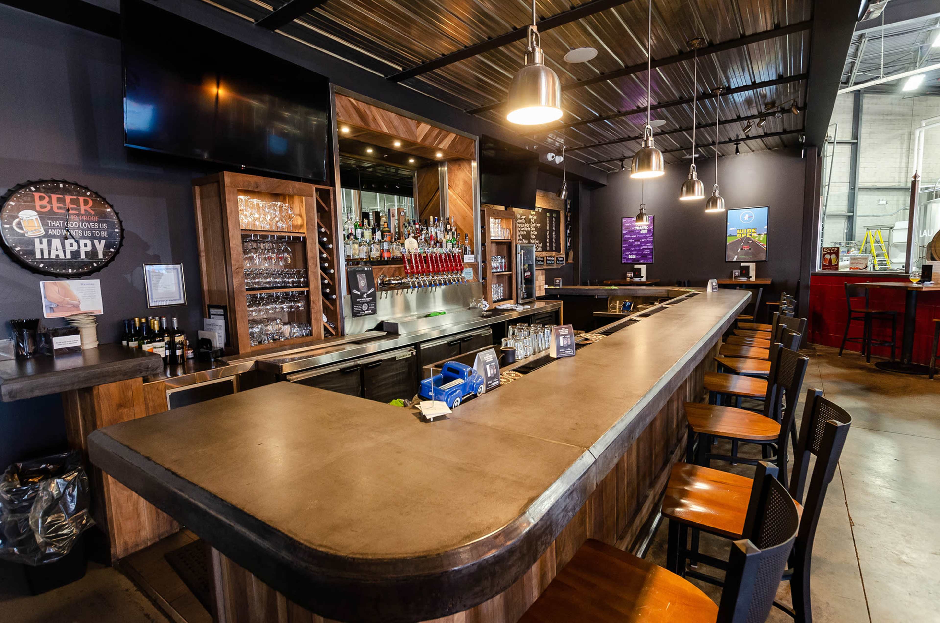 A modern bar with a concrete countertop, wooden accents, and an array of drink taps behind the counter.