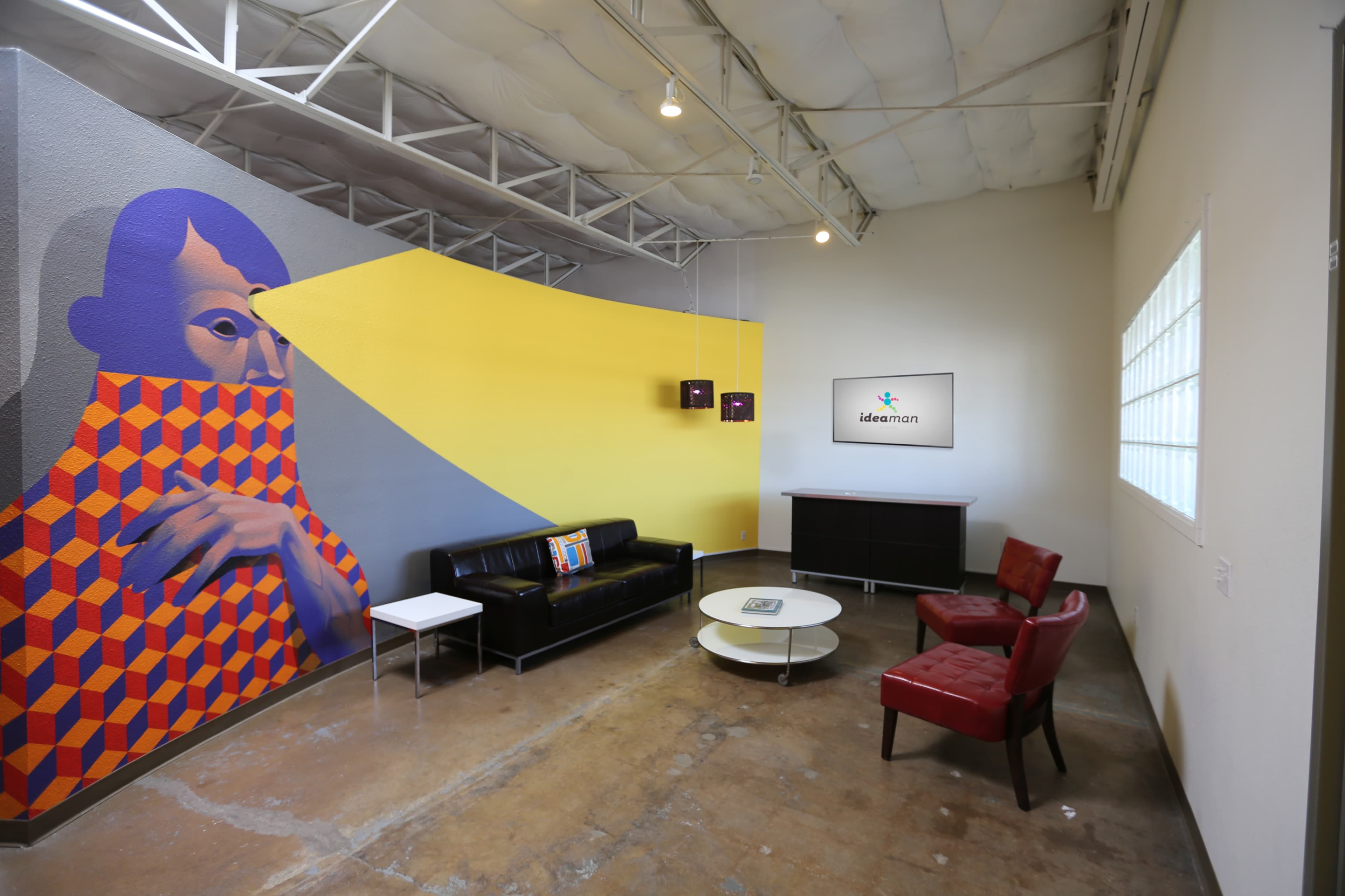 A modern workspace with a colorful mural on one wall, a black sofa, a red armchair, and a low coffee table.