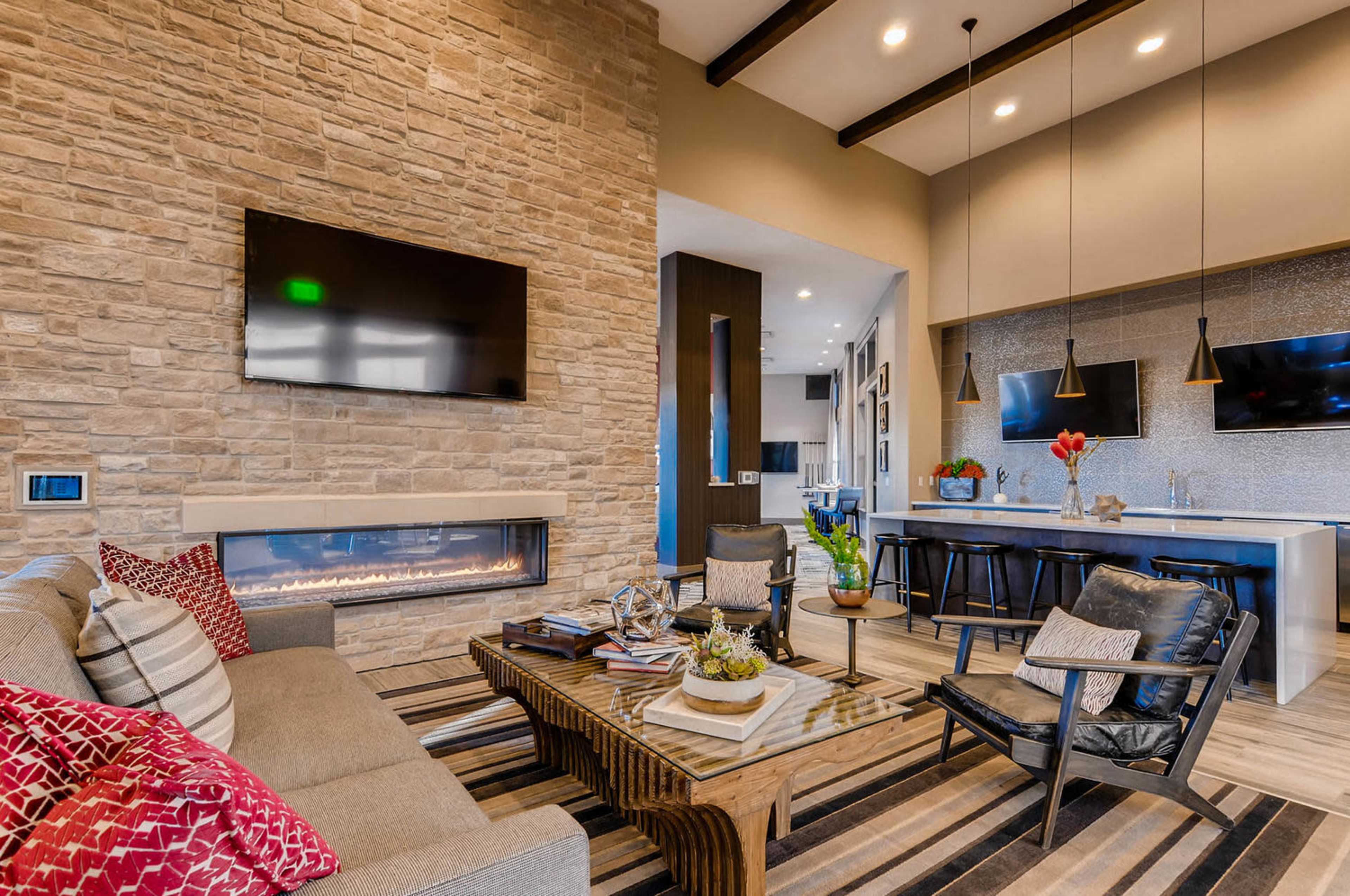 A modern living room with a stone accent wall, a mounted television, a linear fireplace, and a dining area featuring a central table and two pendant lights.