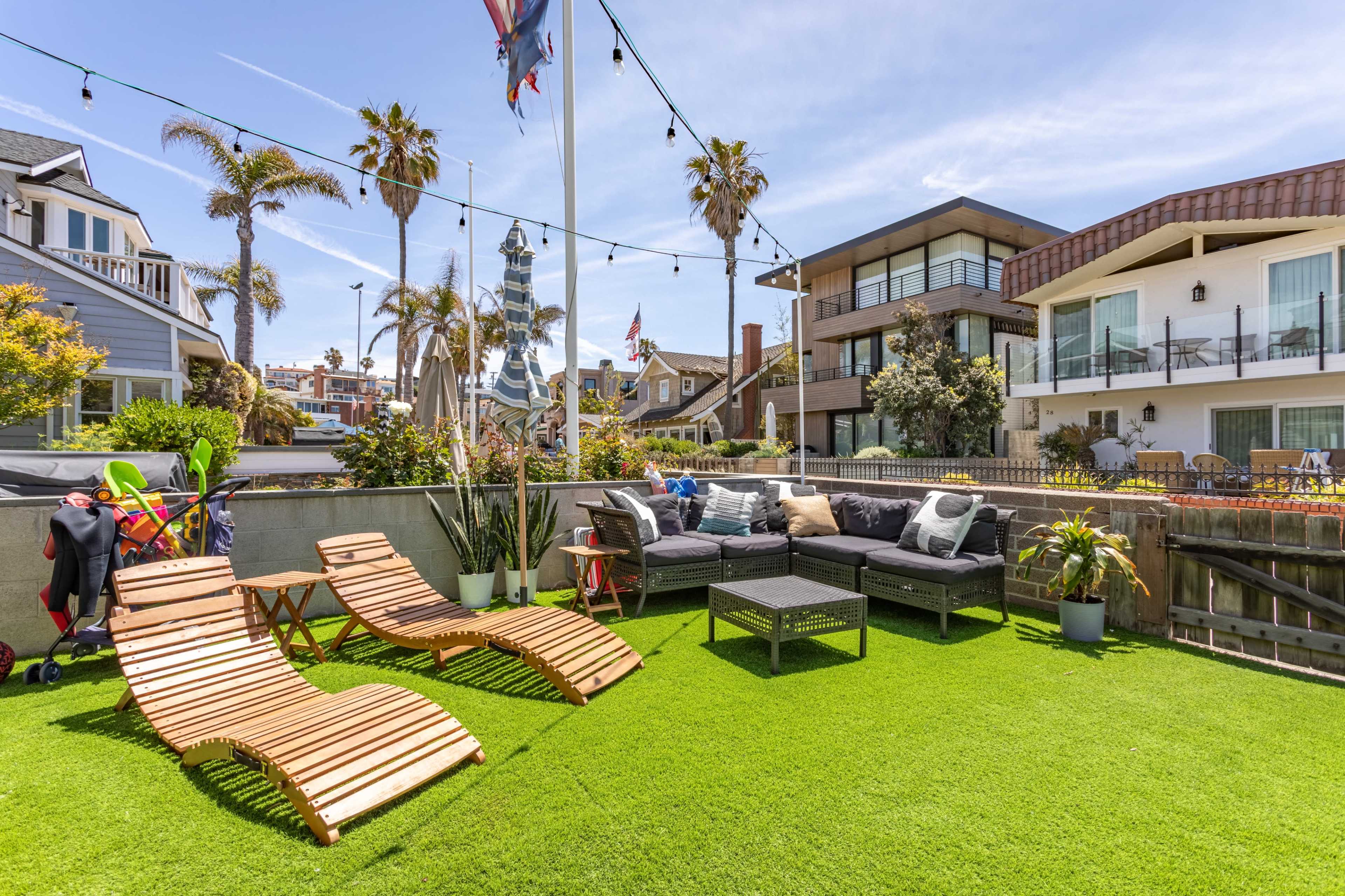 A landscaped outdoor patio featuring lounge chairs and a seating area, surrounded by palm trees and modern buildings.