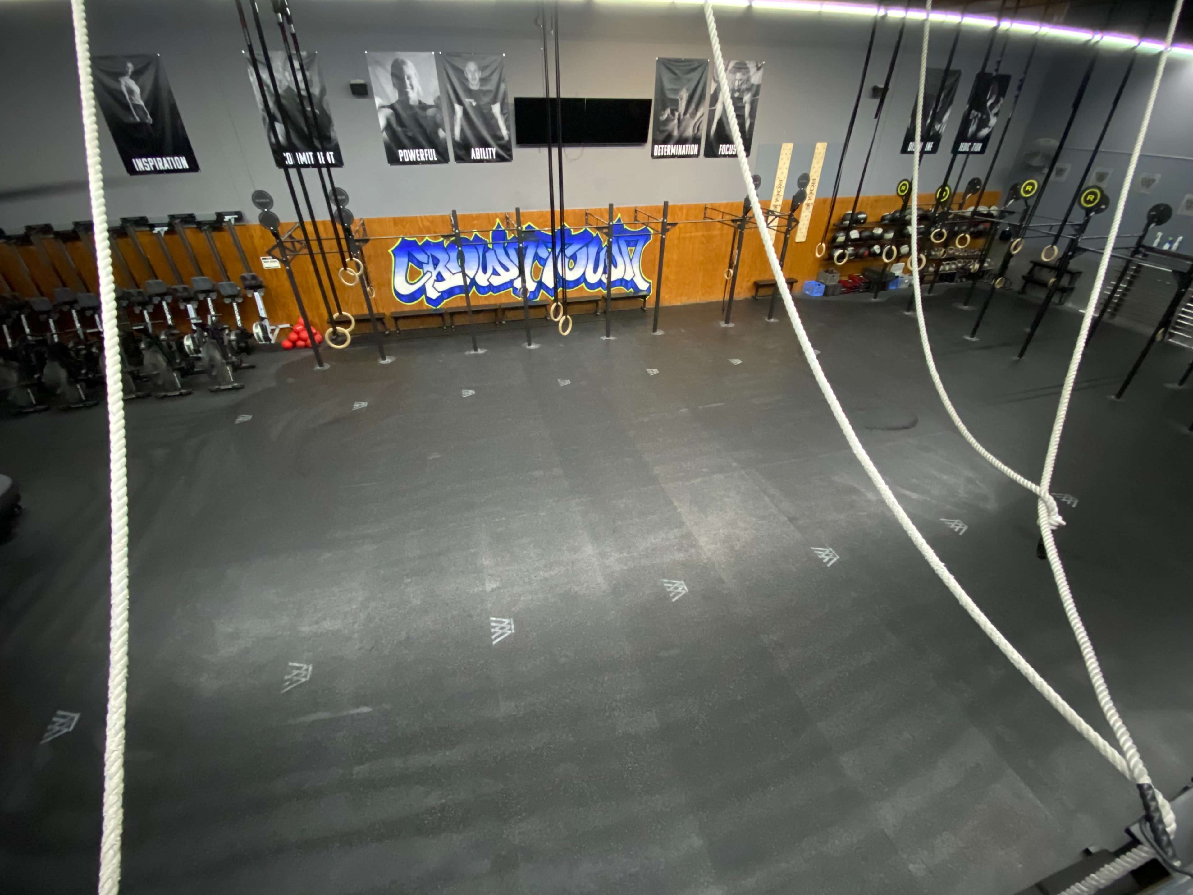 A gym interior with exercise equipment, a colorful mural, and hanging ropes and rings.