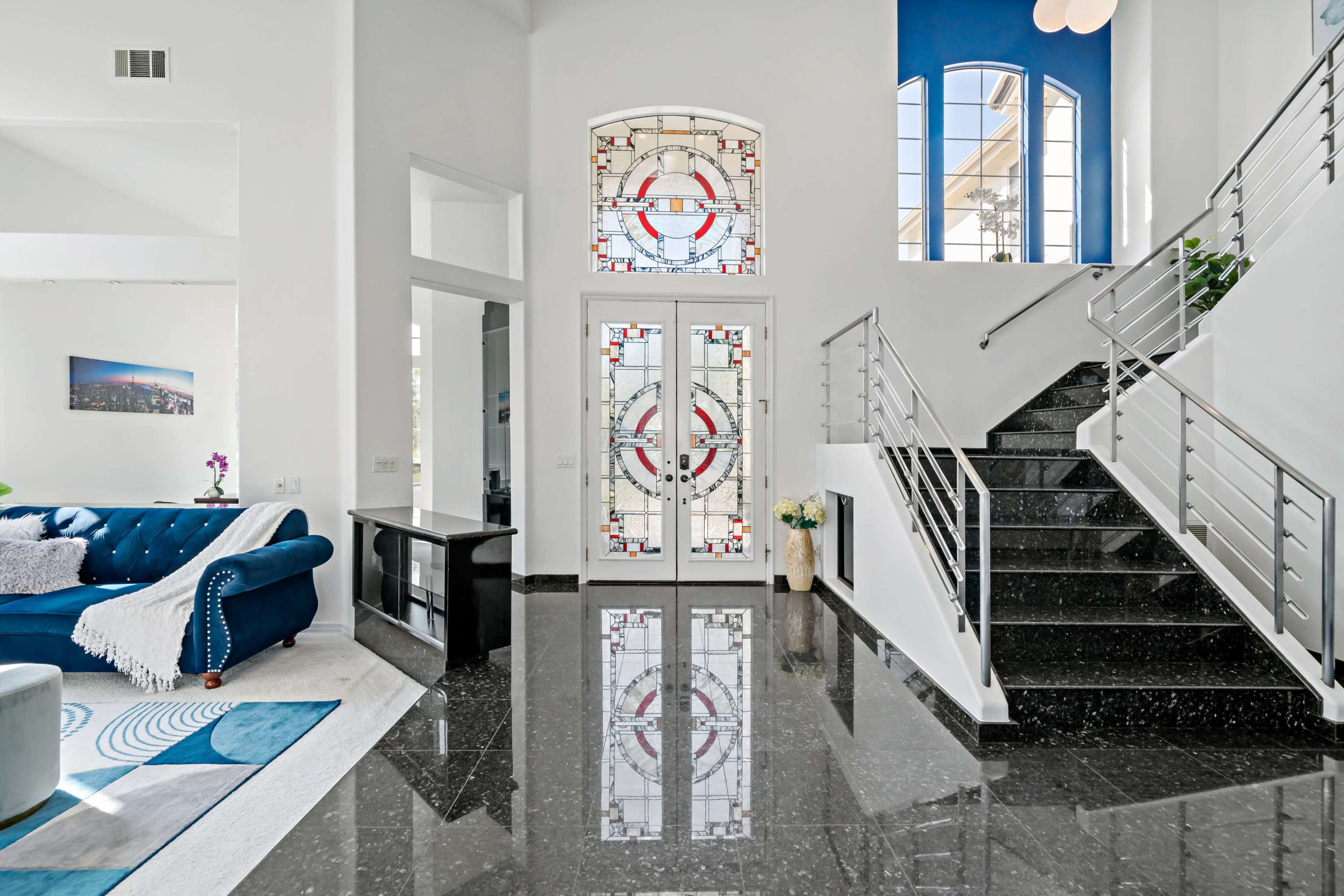 A modern entryway with stained glass doors, a staircase, and polished black floor tiles.