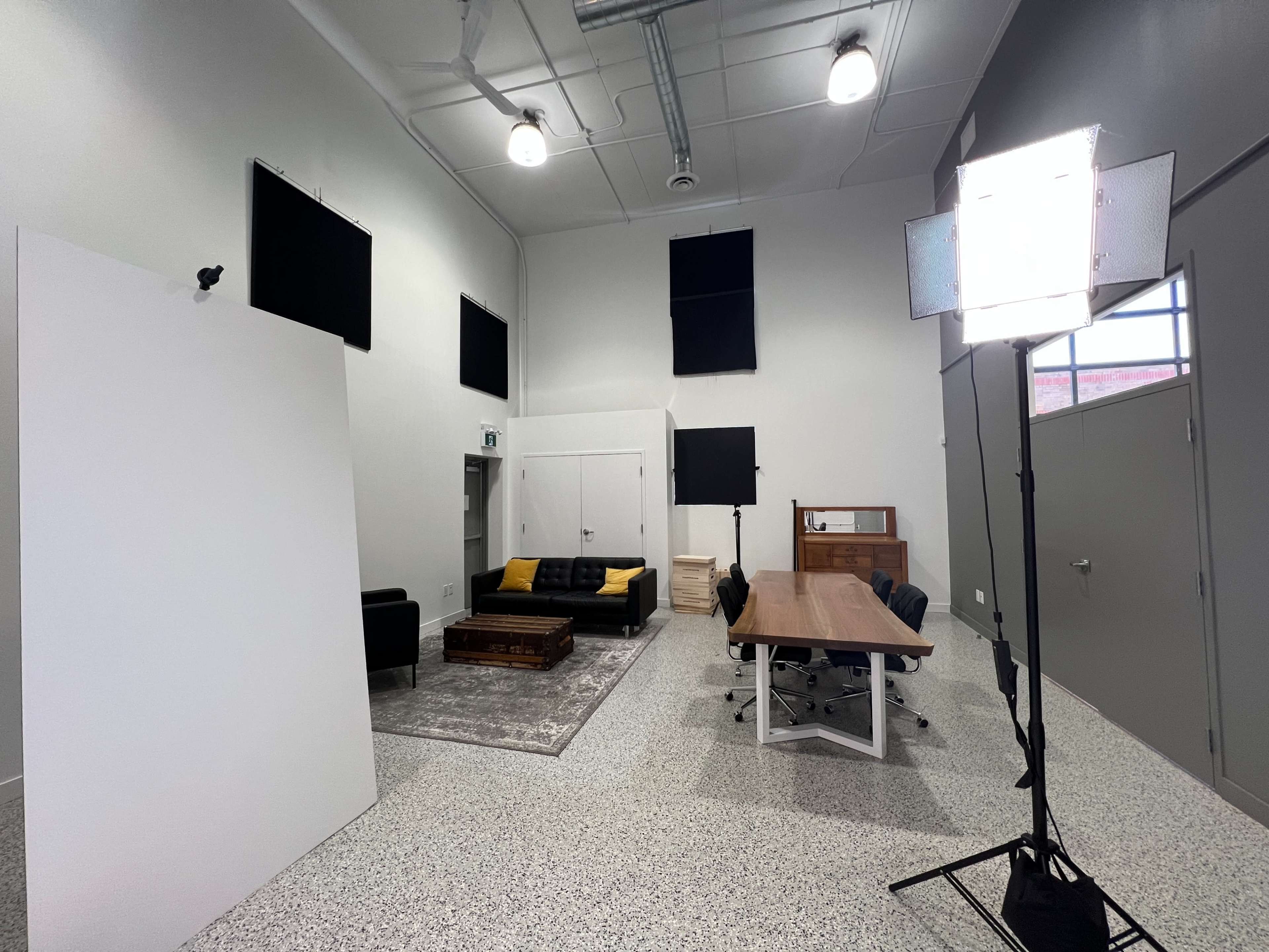 A spacious studio with a seating area, a large table, and multiple lighting setups on a light-colored floor.
