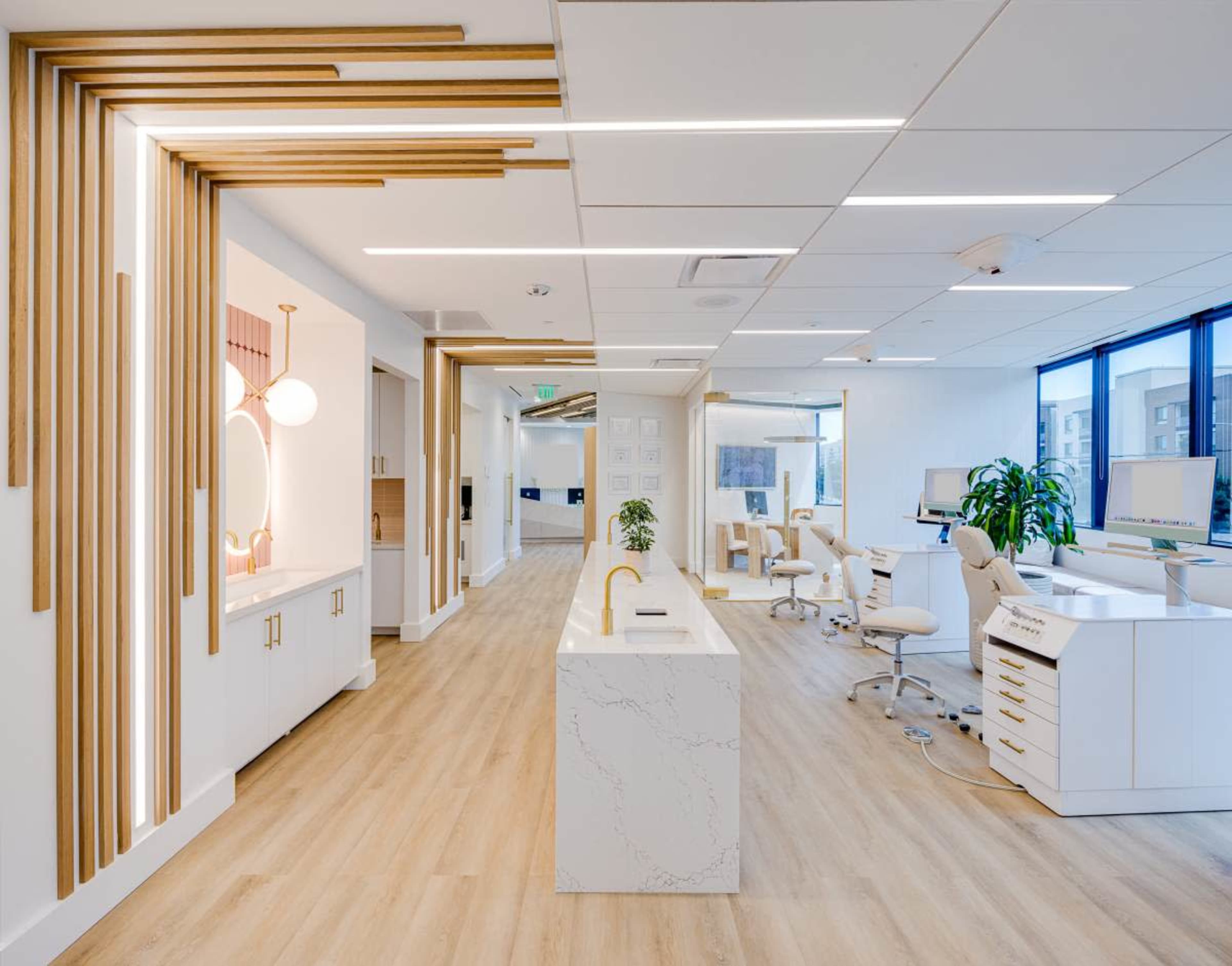 The image shows a modern, well-lit dental office with wooden accents, a reception area, and dental equipment arranged along the walls.