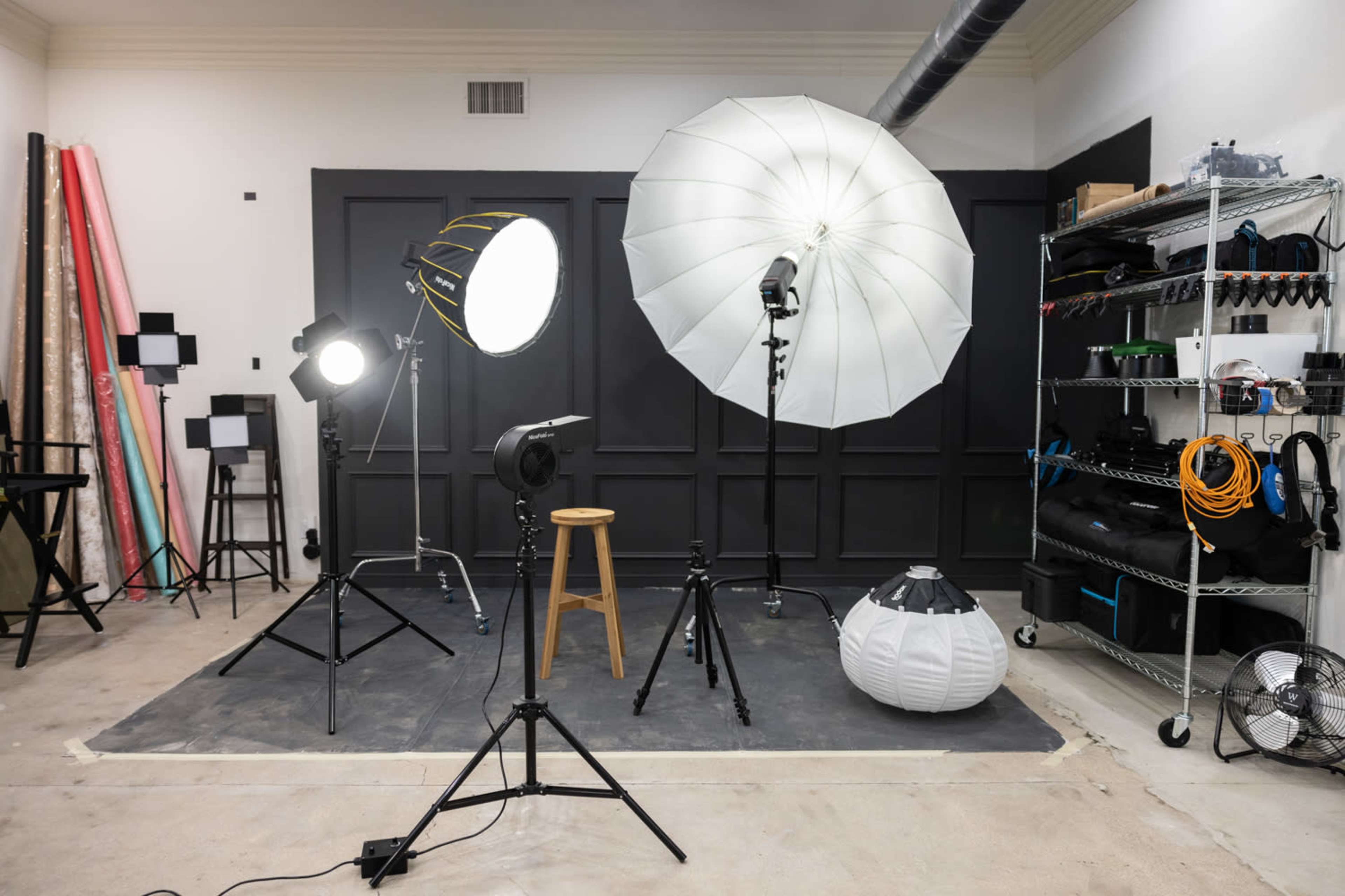 A photography studio setup with various lighting equipment, a stool, and backdrops arranged against a black wall.