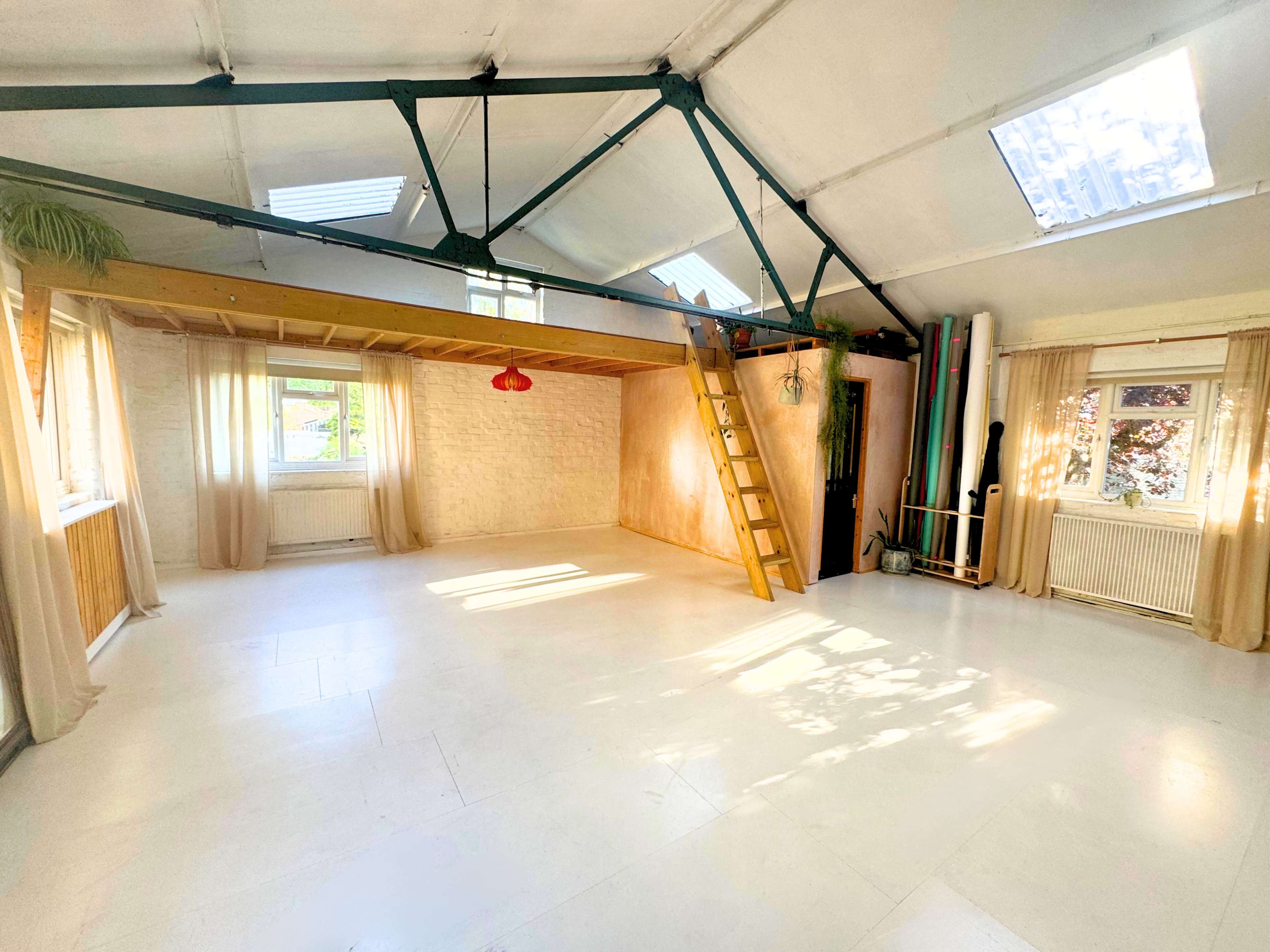 A spacious, well-lit room with a loft area, wooden ladder, and large windows.