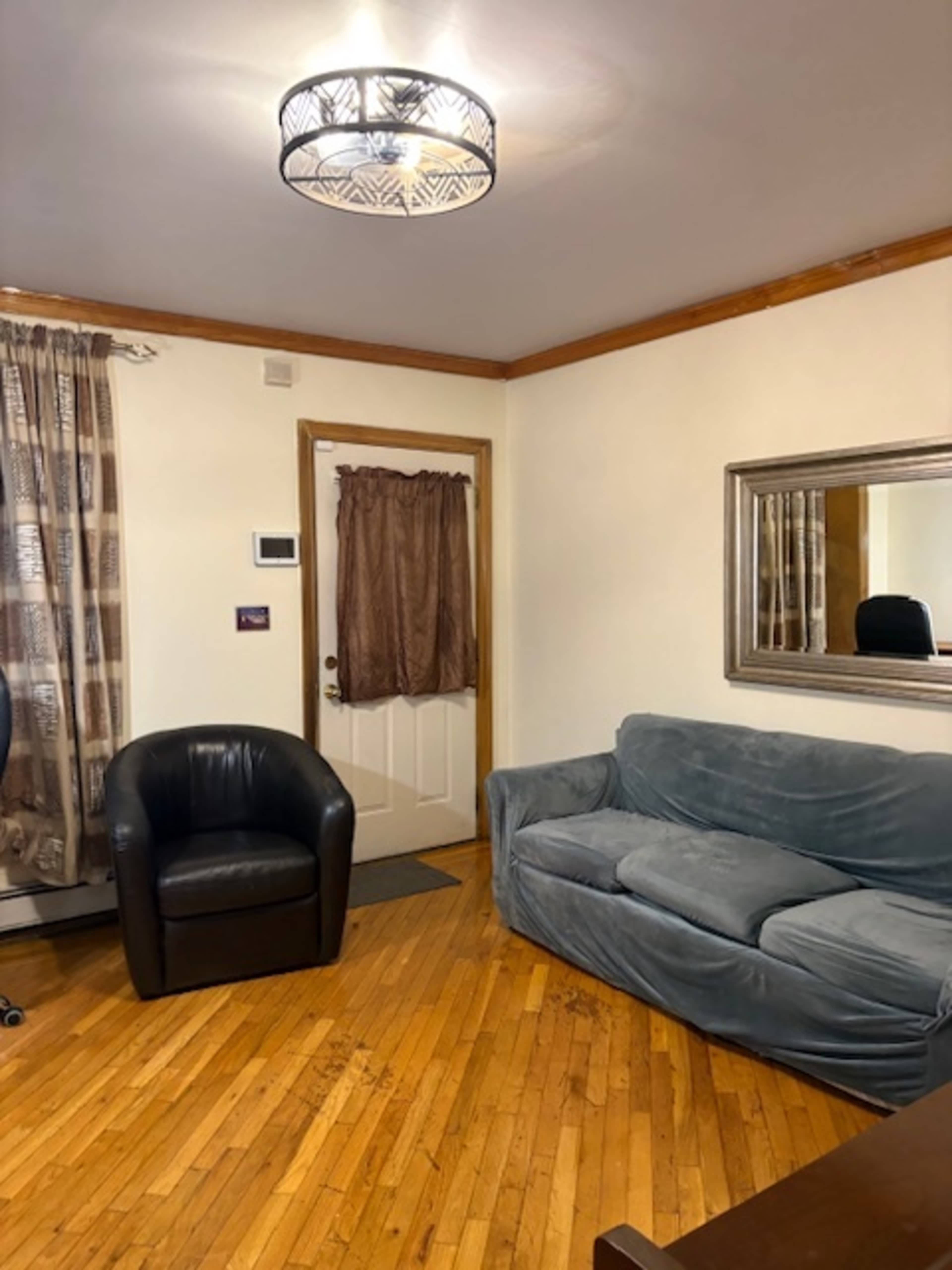The image shows a living room with a blue couch, a black armchair, a door with a brown curtain, and a large mirror on the wall.