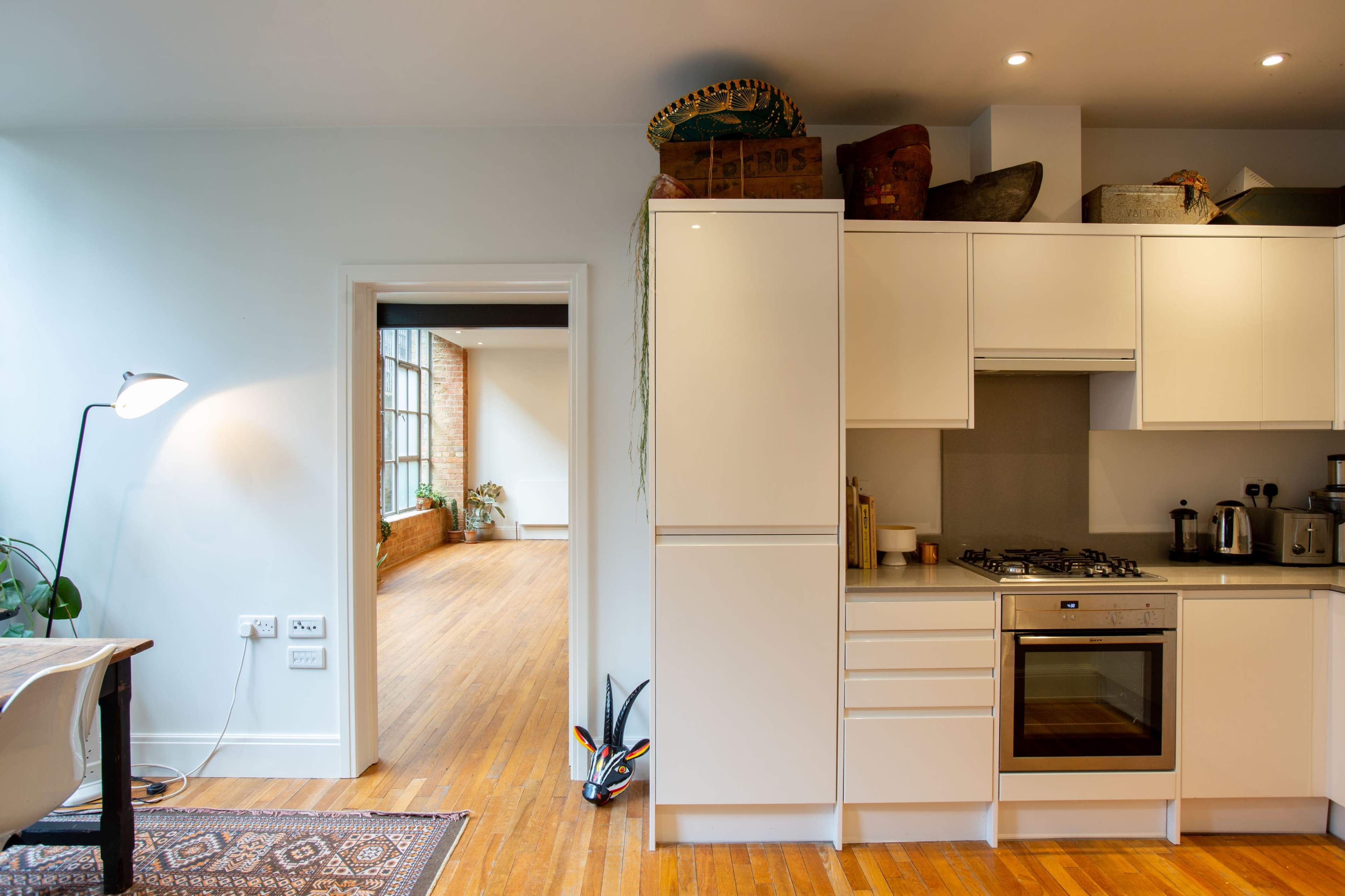 A modern kitchen with white cabinetry and a doorway leading to a bright, open room with hardwood floors.