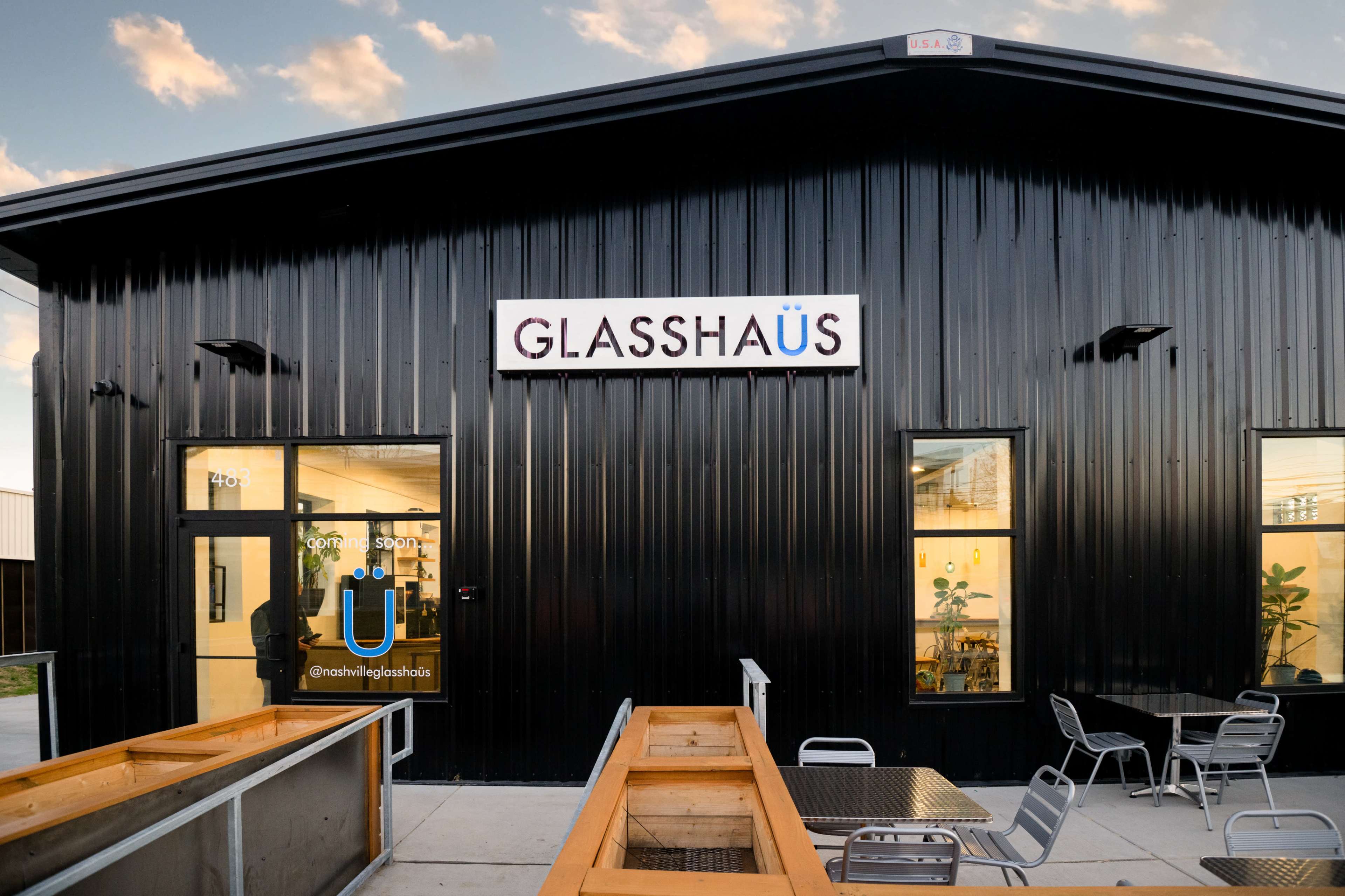 The image shows the exterior of a modern, black metal building with large windows and a sign labeled "GLASSHAUS."