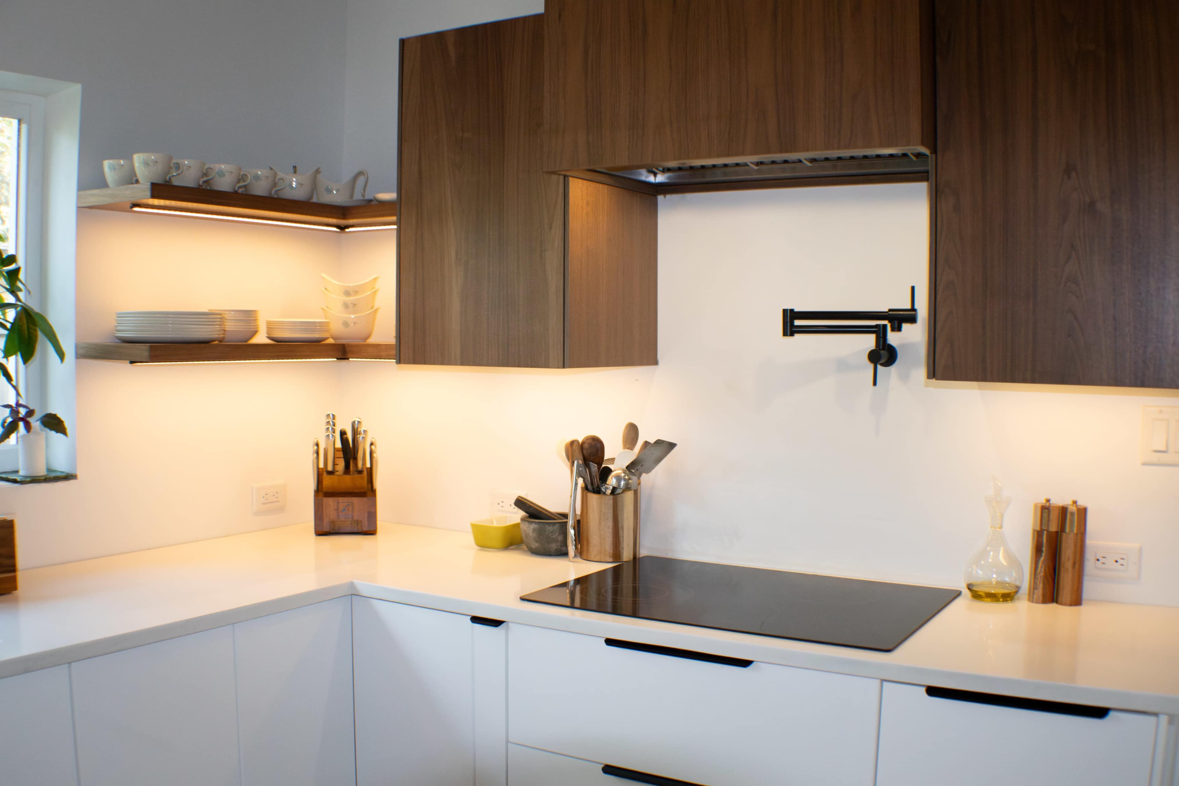 A modern kitchen with wooden cabinetry, a flat cooktop, and neatly arranged kitchen utensils on the counter and shelves.