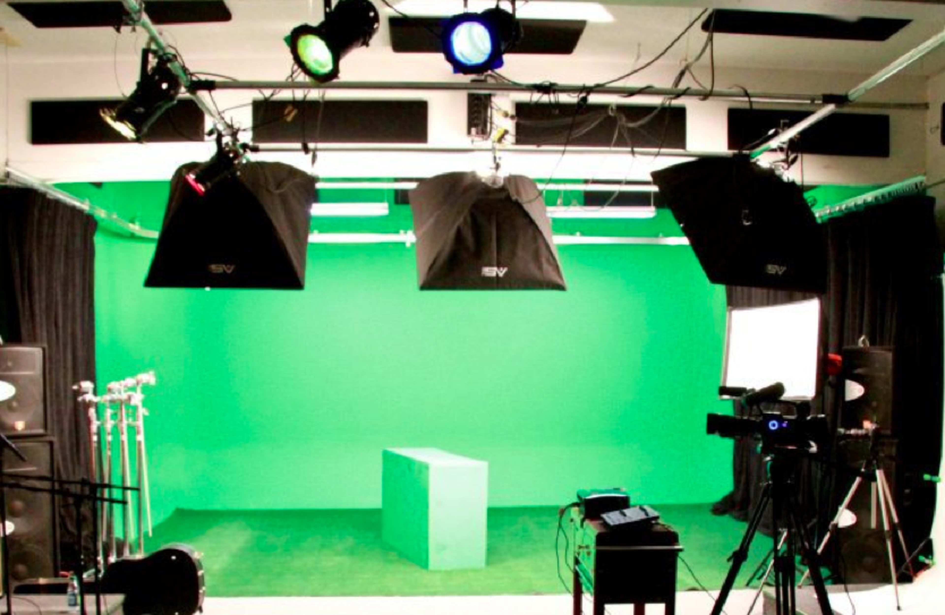 The image shows a green screen studio setup with lighting, a green box in the center, and various cameras and equipment arranged around the space.