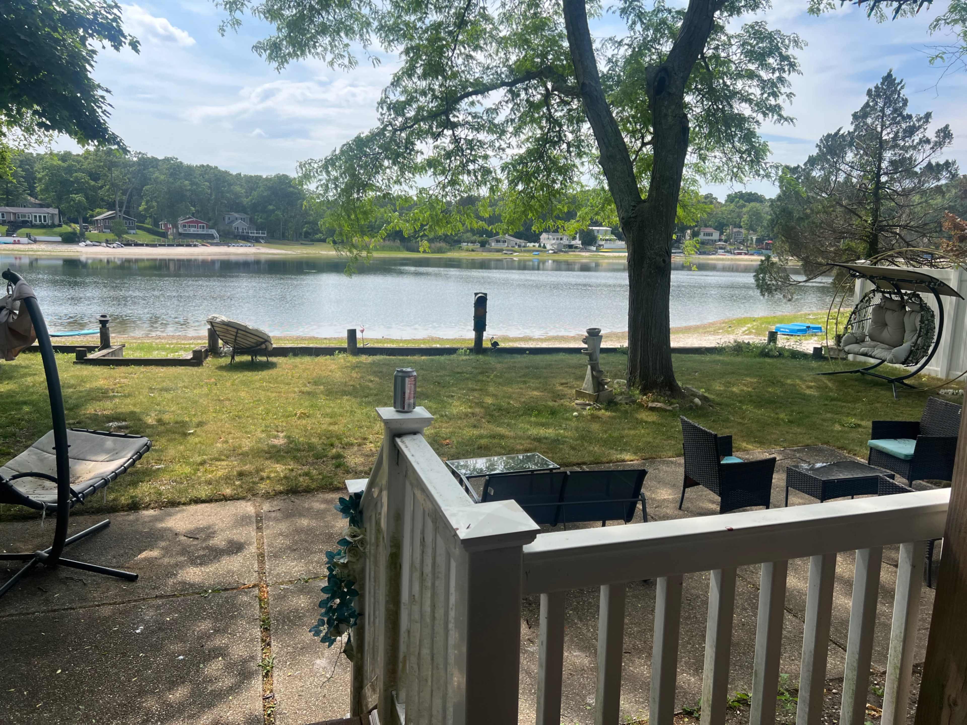 The image shows a serene lakeside view from a patio, with several outdoor seating arrangements and a grassy area leading to the water.