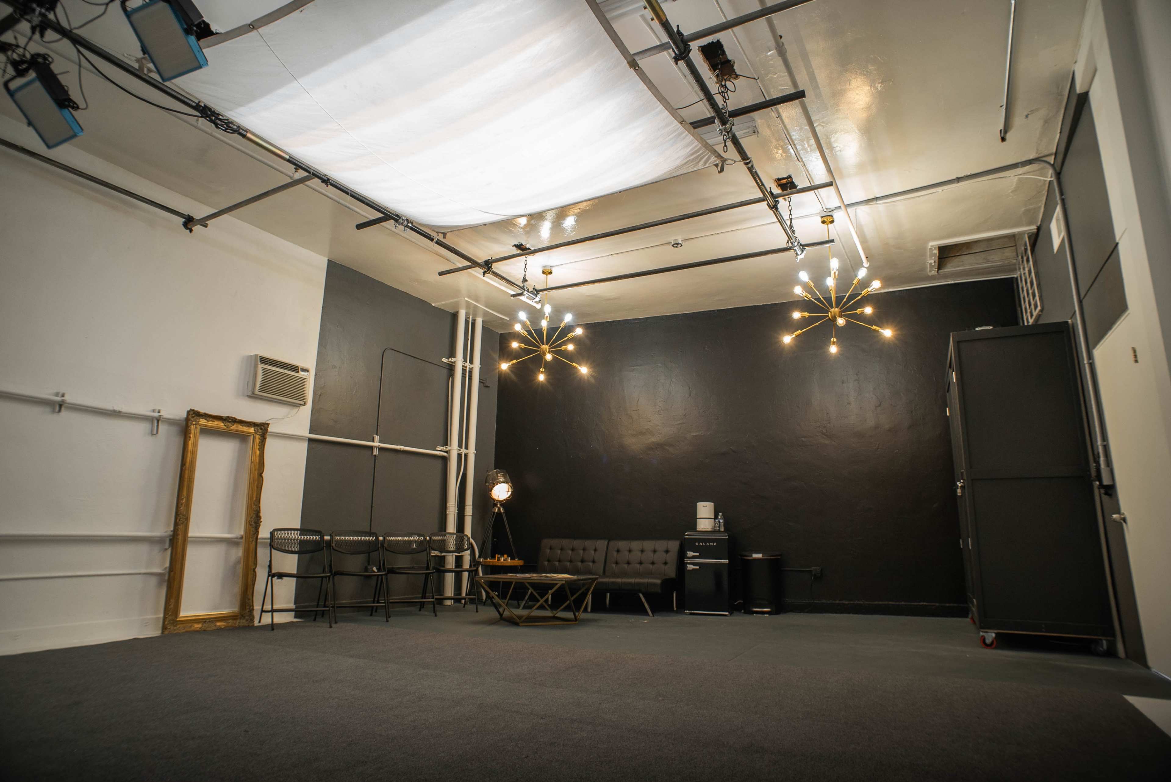 A spacious, minimalist studio with a dark wall, two light fixtures, a couch, a coffee table, and a closet.