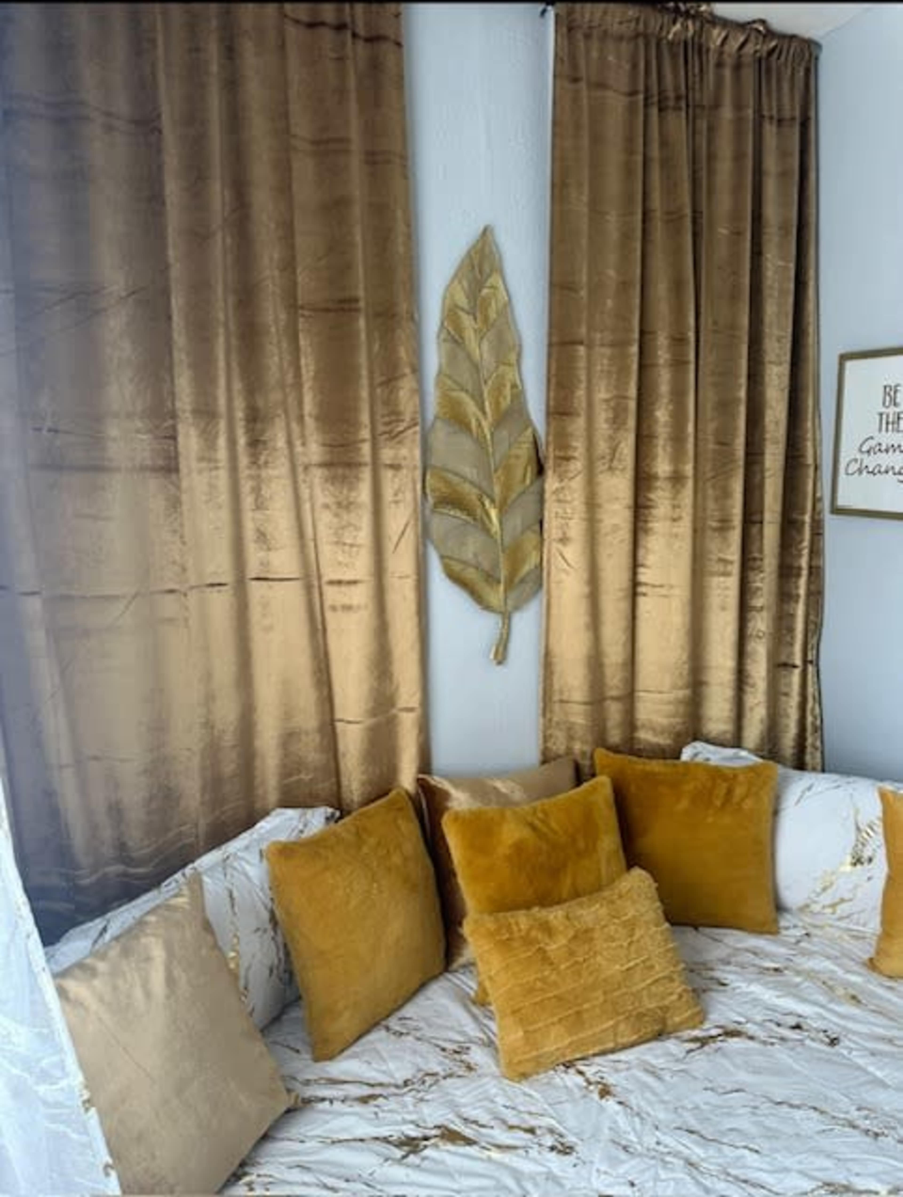 A cozy corner features a marble-patterned seating area adorned with several golden-yellow pillows and luxurious golden curtains.