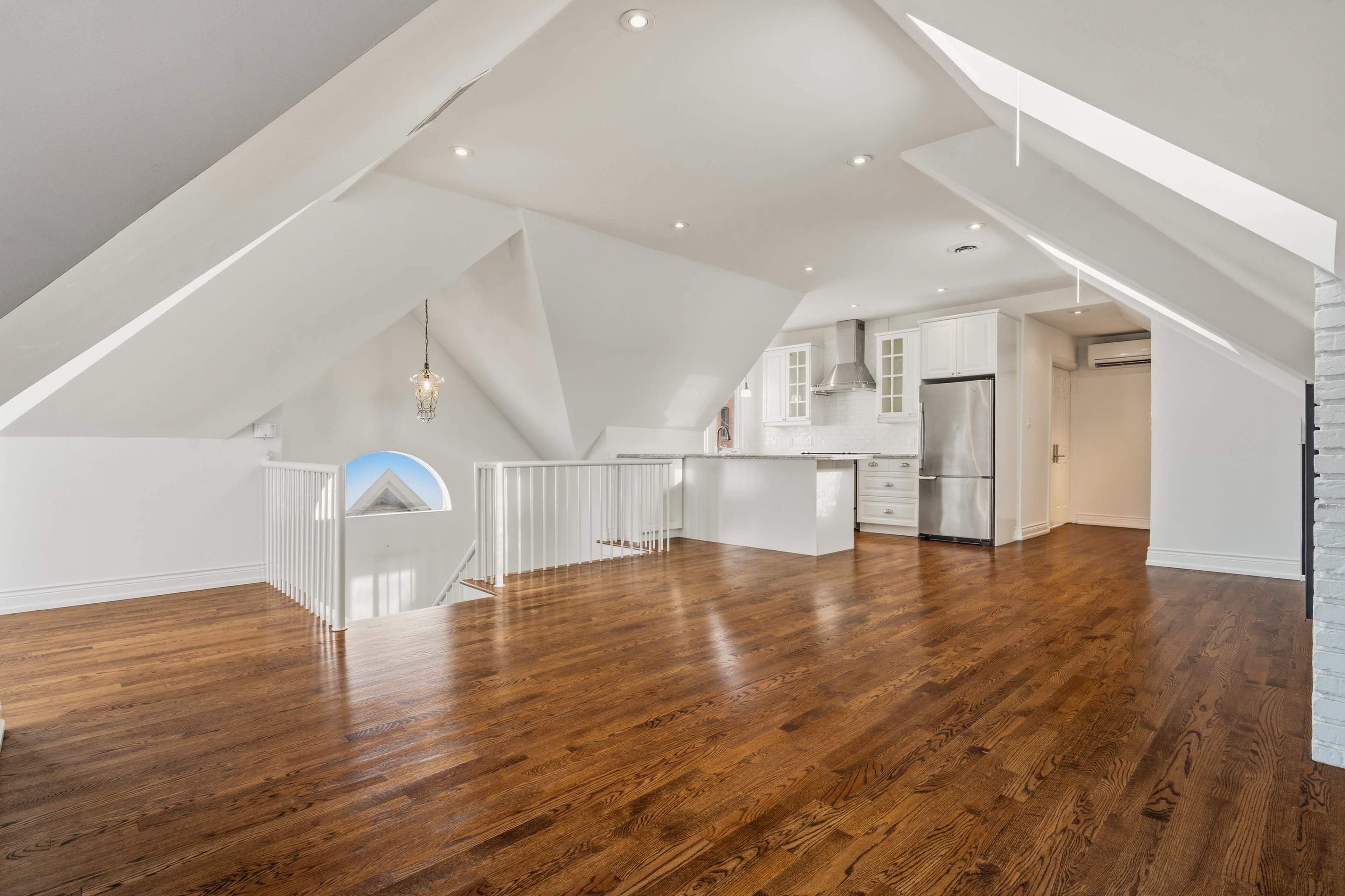 The image shows a spacious, bright attic with sloped ceilings, hardwood flooring, and an open kitchen area.