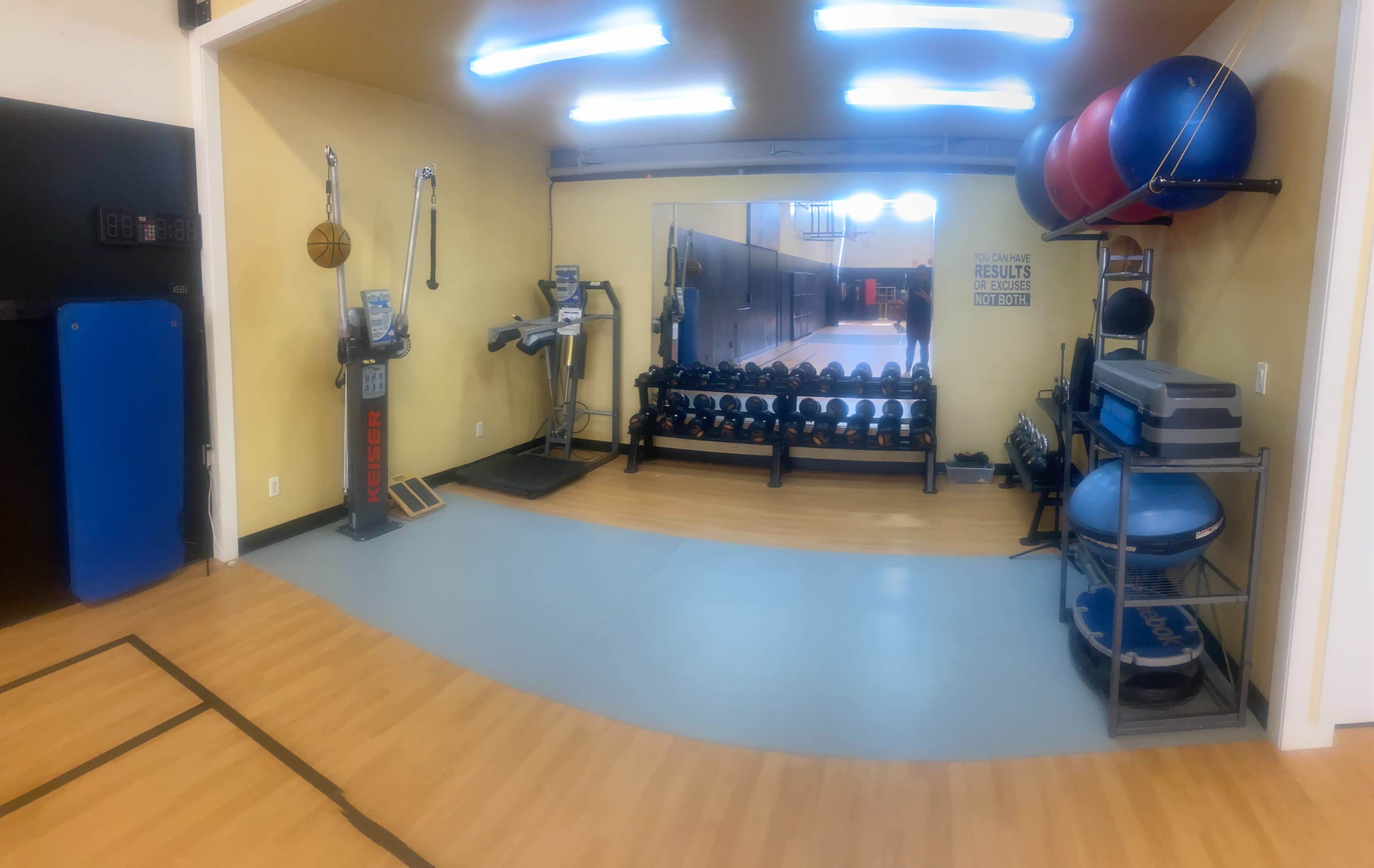 A well-equipped gym area featuring a row of dumbbells, exercise machines, and fitness equipment arranged along the walls.