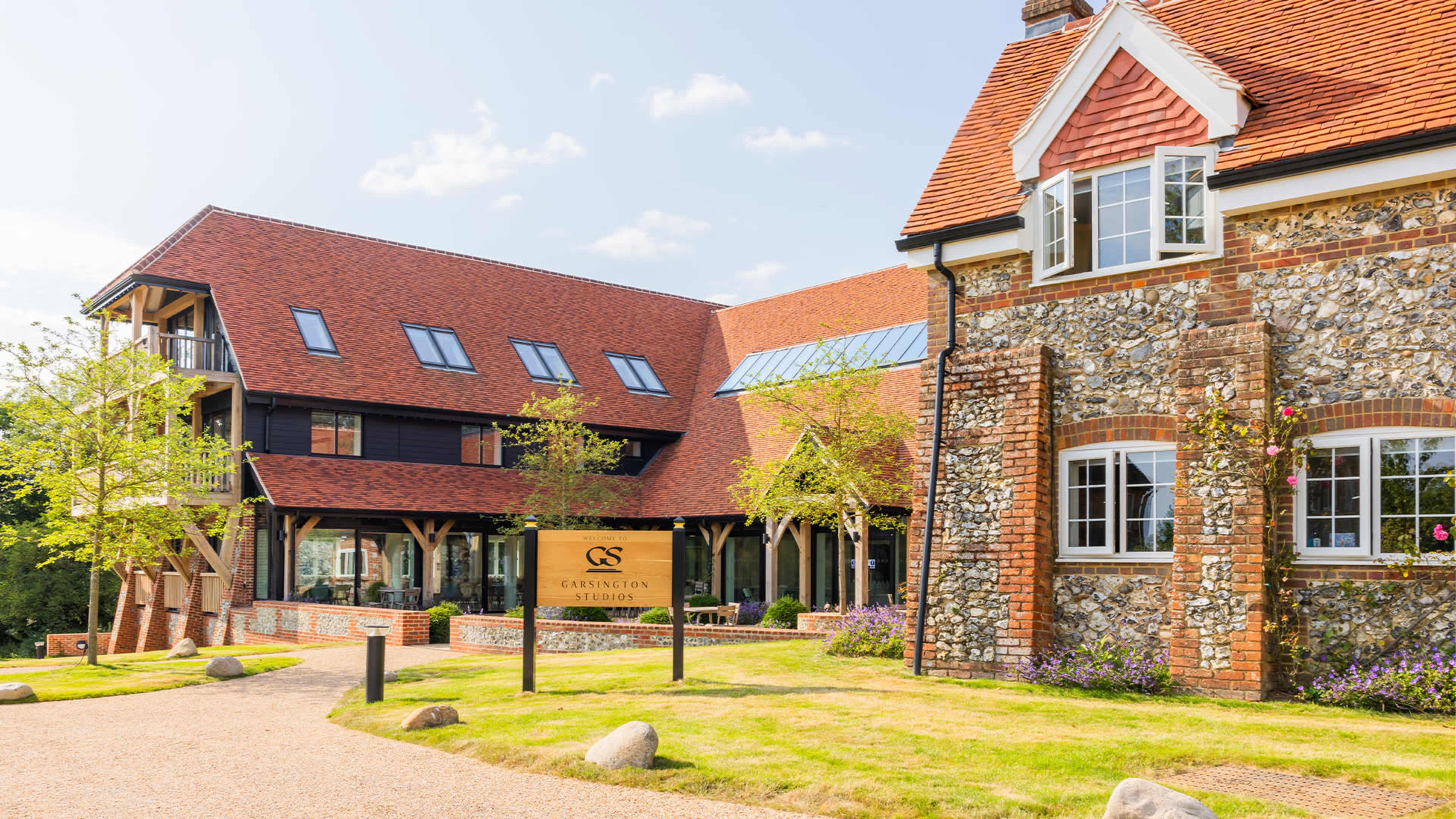 A modern hotel building with a stone and timber structure, surrounded by greenery and a gravel path leading to the entrance.
