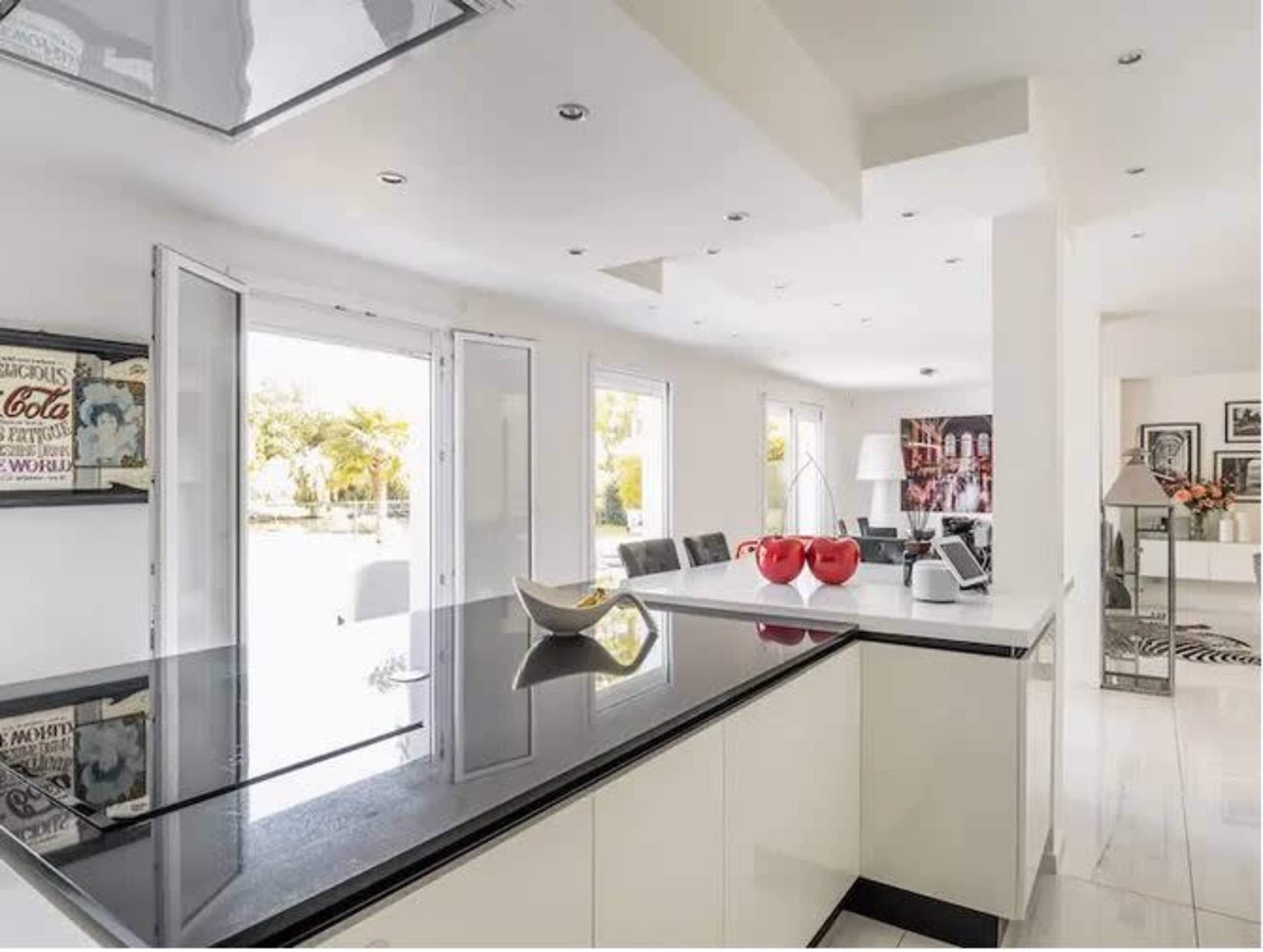 The image shows a modern kitchen with a black countertop, white cabinetry, and large open doors leading to an outdoor area.