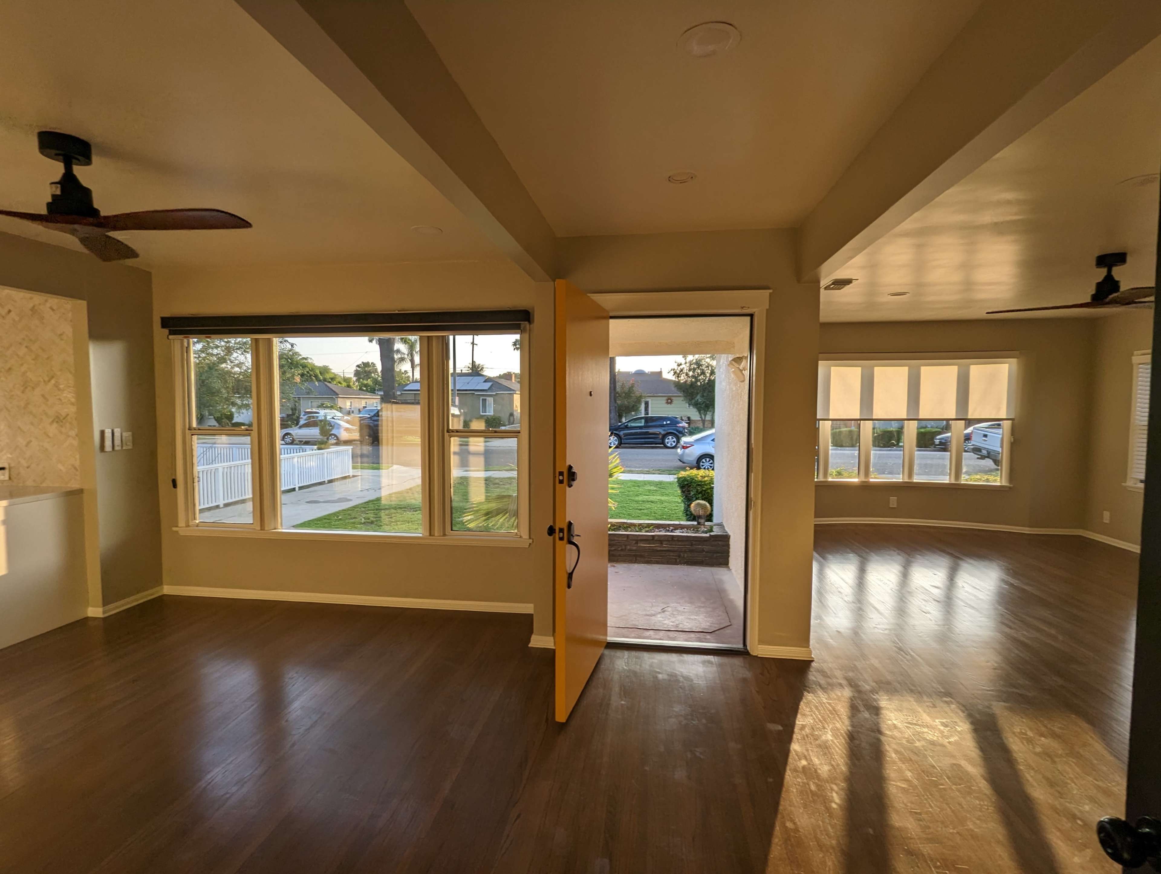 The image shows a brightly lit interior space with an open doorway leading to a front yard, while large windows allow natural light to fill the room.