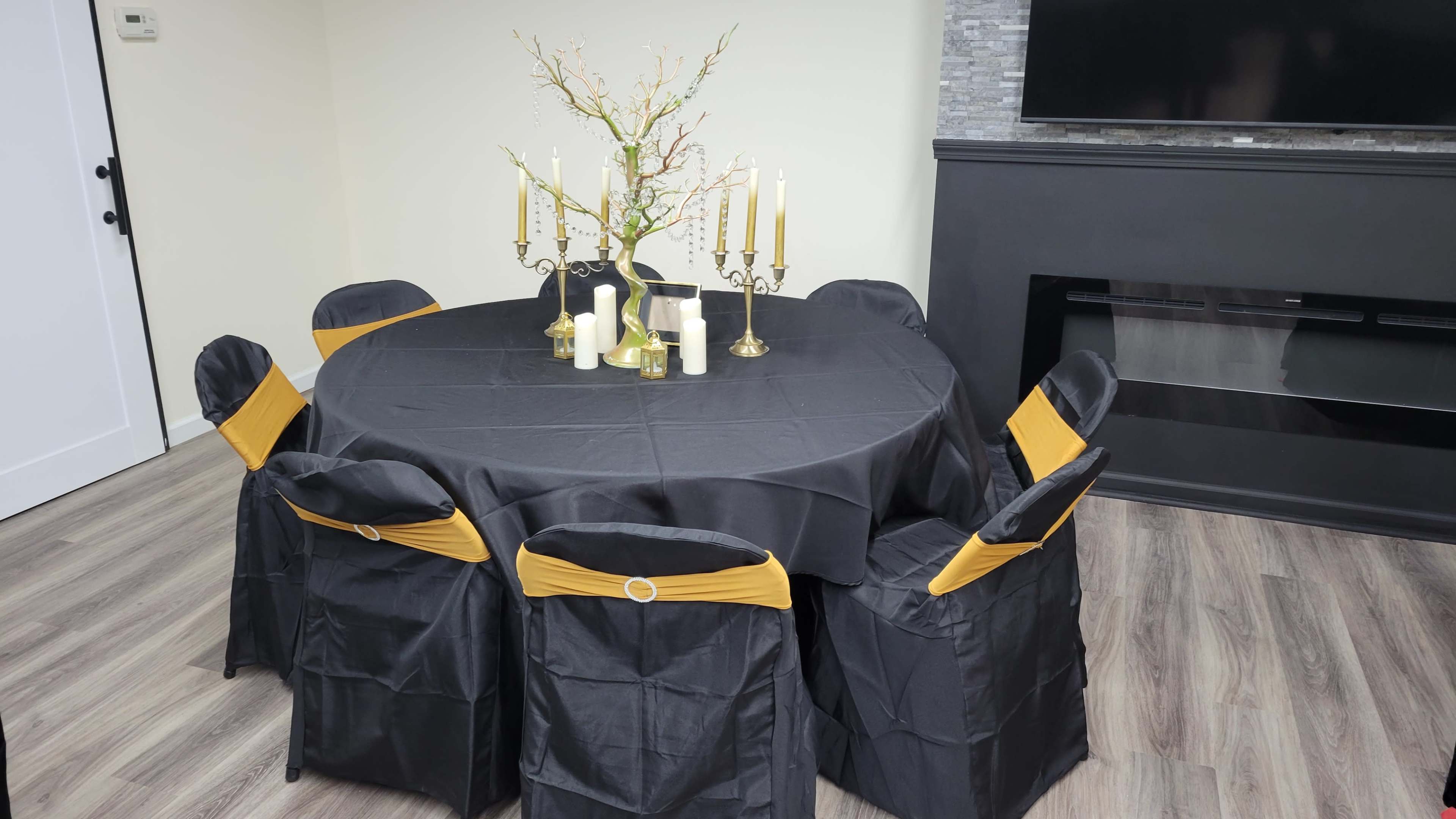 A round table covered with a black tablecloth and adorned with gold accents is surrounded by chairs dressed in black covers with yellow sashes.