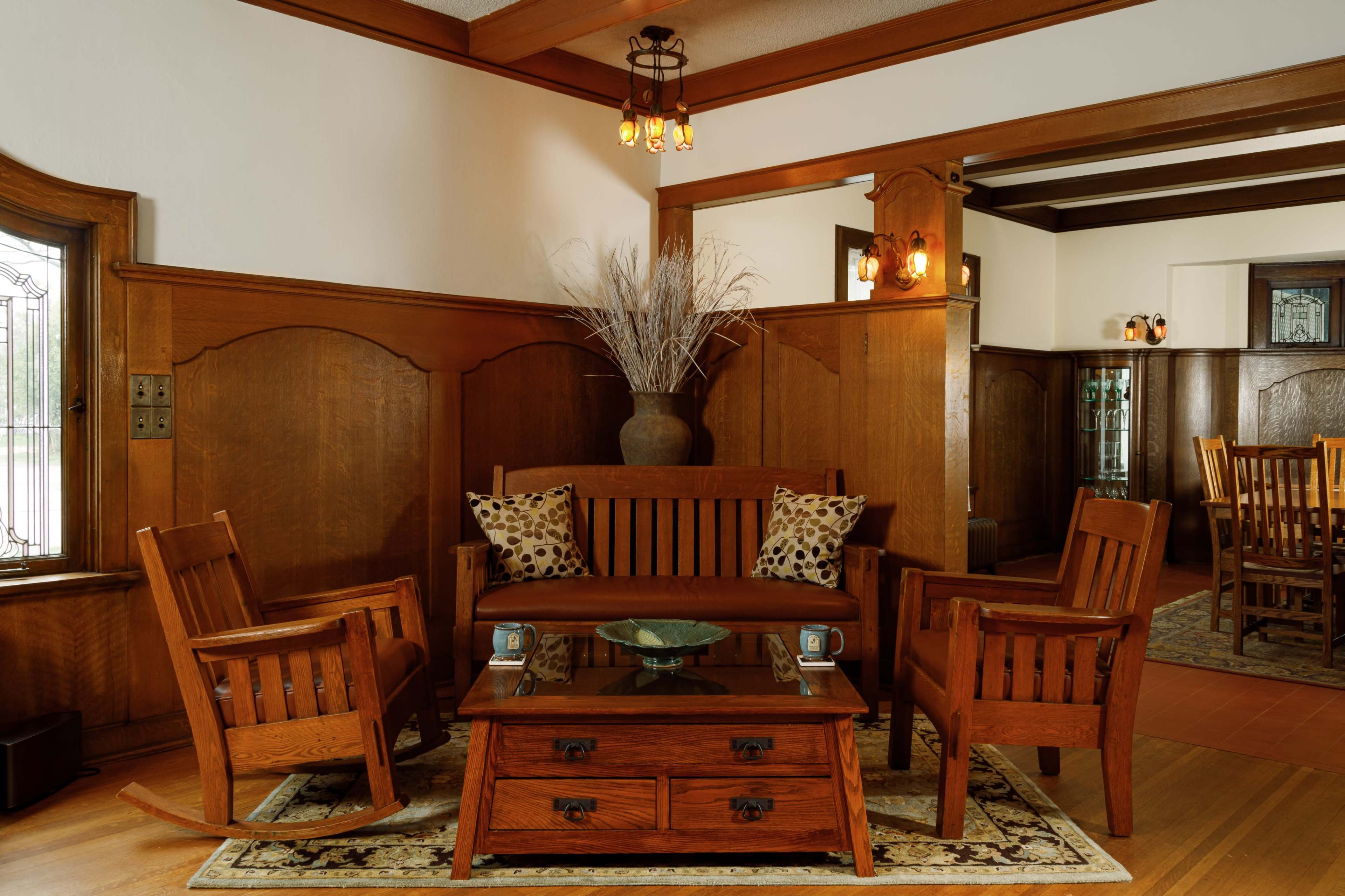 A wooden living room with a set of matching furniture, including a sofa, two rocking chairs, and a glass-top coffee table on a patterned rug.