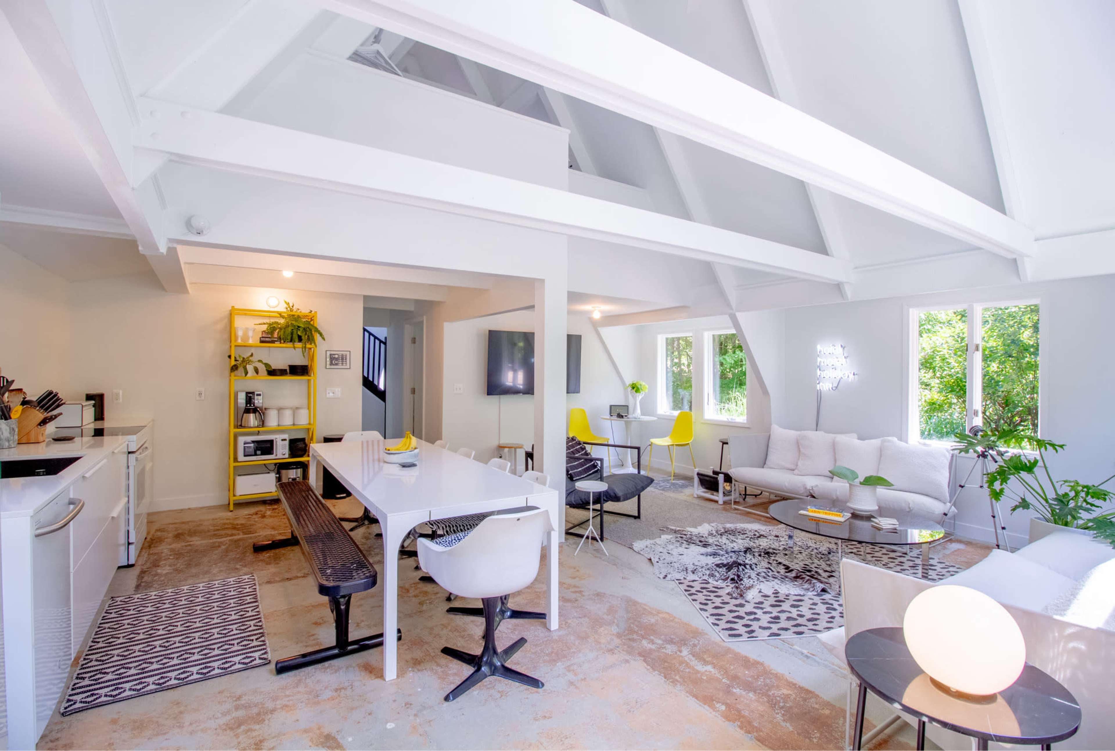 An open-concept living space with a modern kitchen, dining area, and lounge, featuring large windows and a high, sloped ceiling.