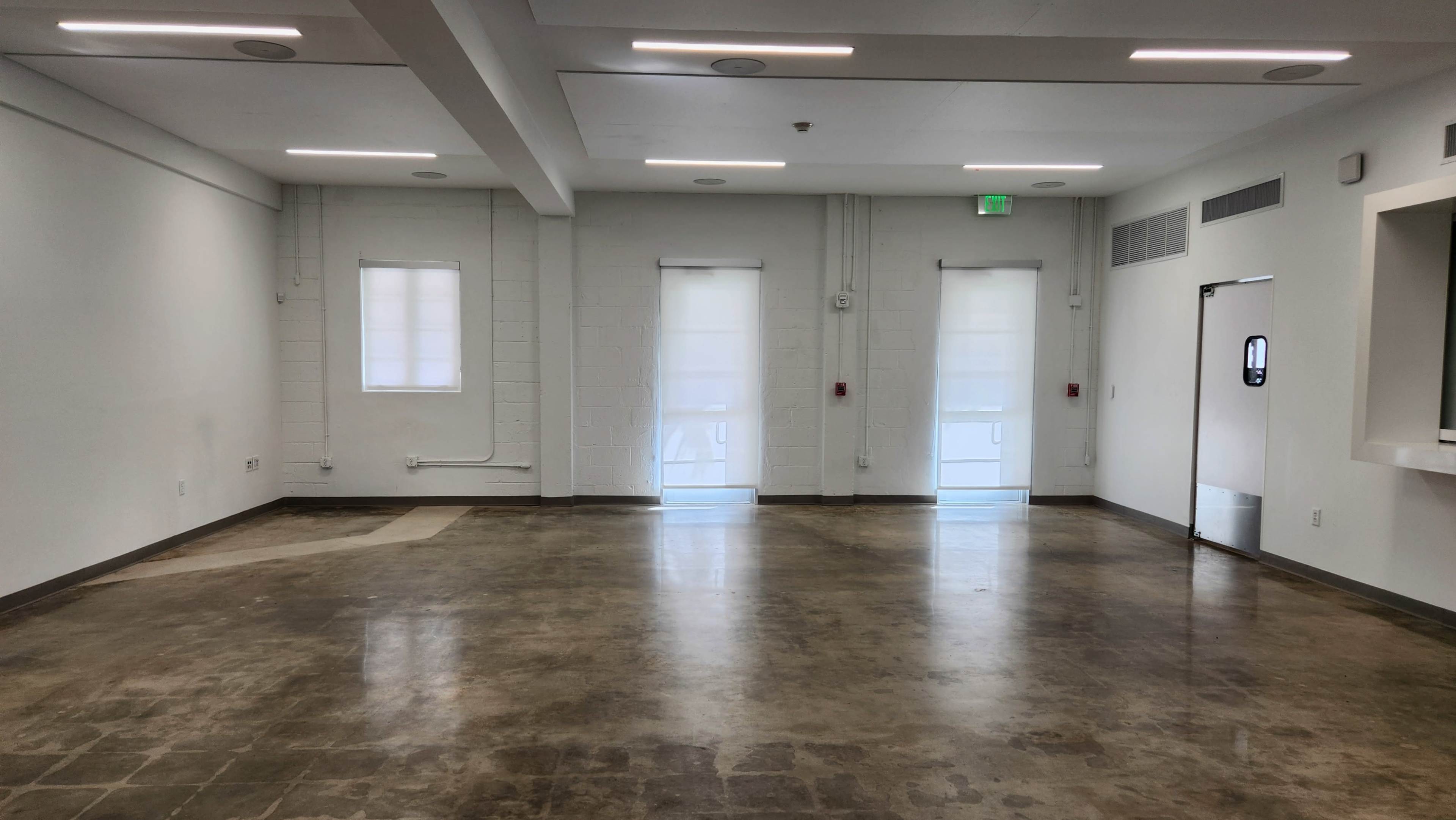 The image shows an empty room with a polished concrete floor, white walls, and two windows with sheer curtains at the far end.