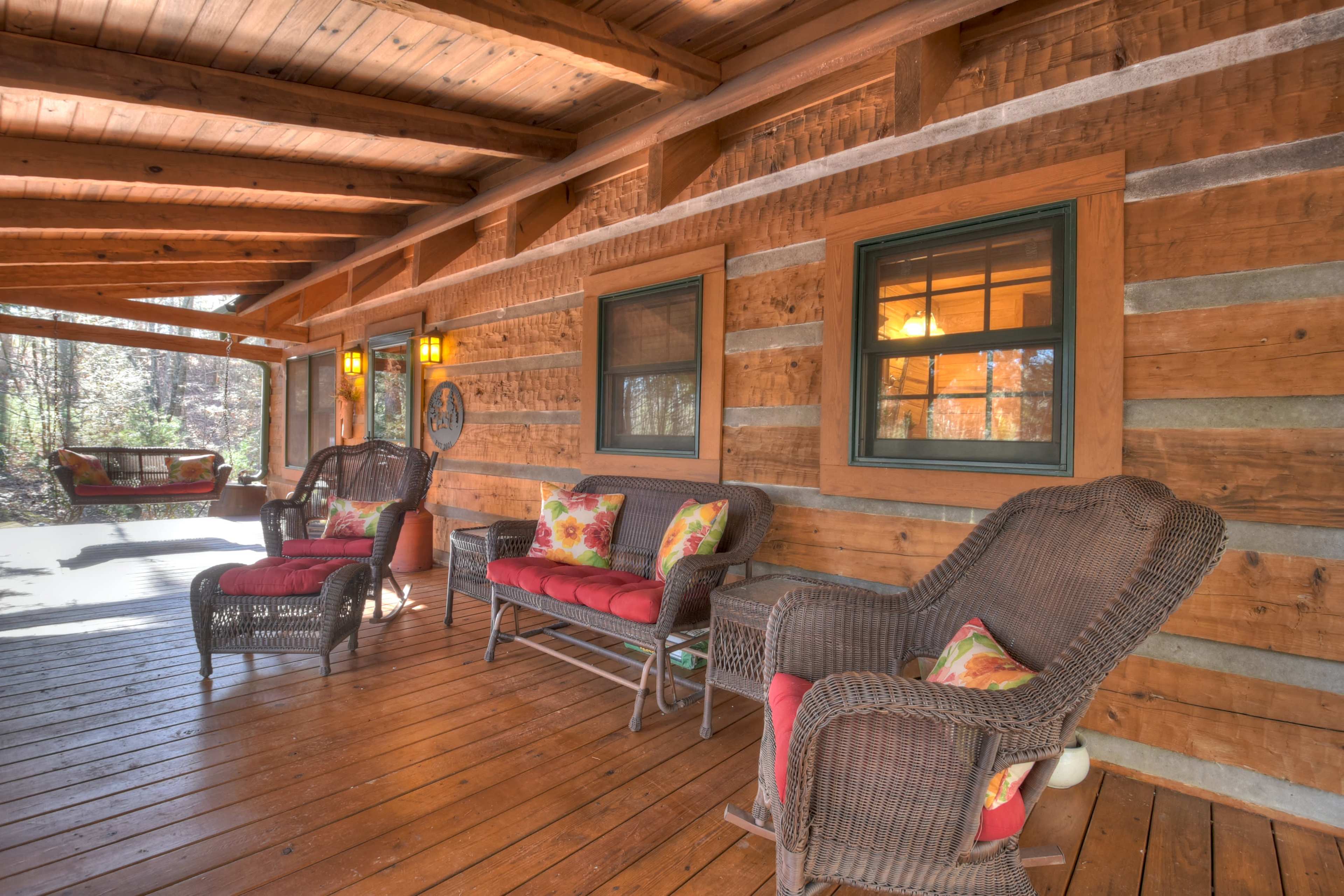 A wooden porch area with log walls, featuring wicker chairs and a swing.