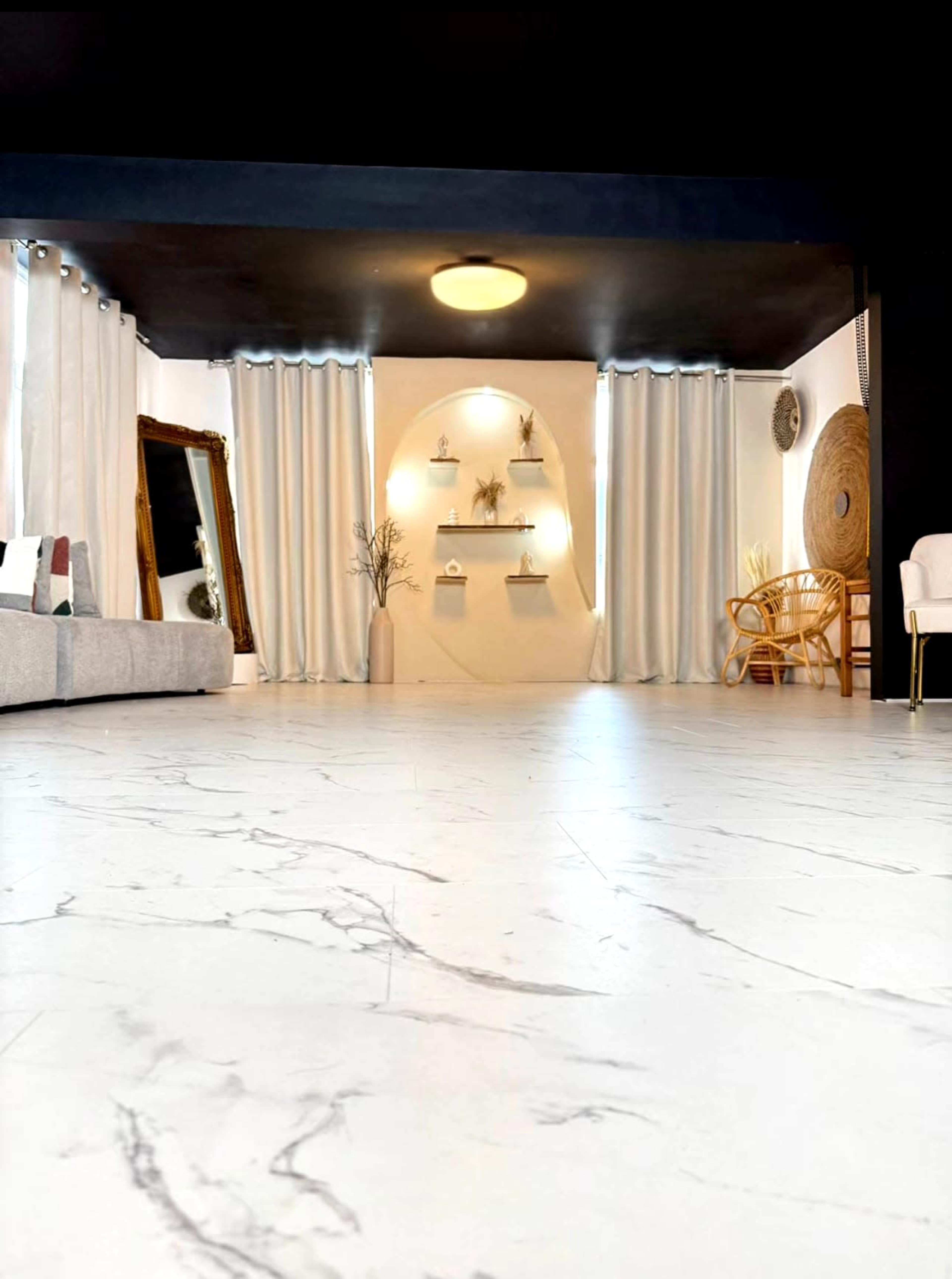 The image shows a modern interior space with a marble floor, large curtains, a mirror, shelves with decor, and minimal furniture.